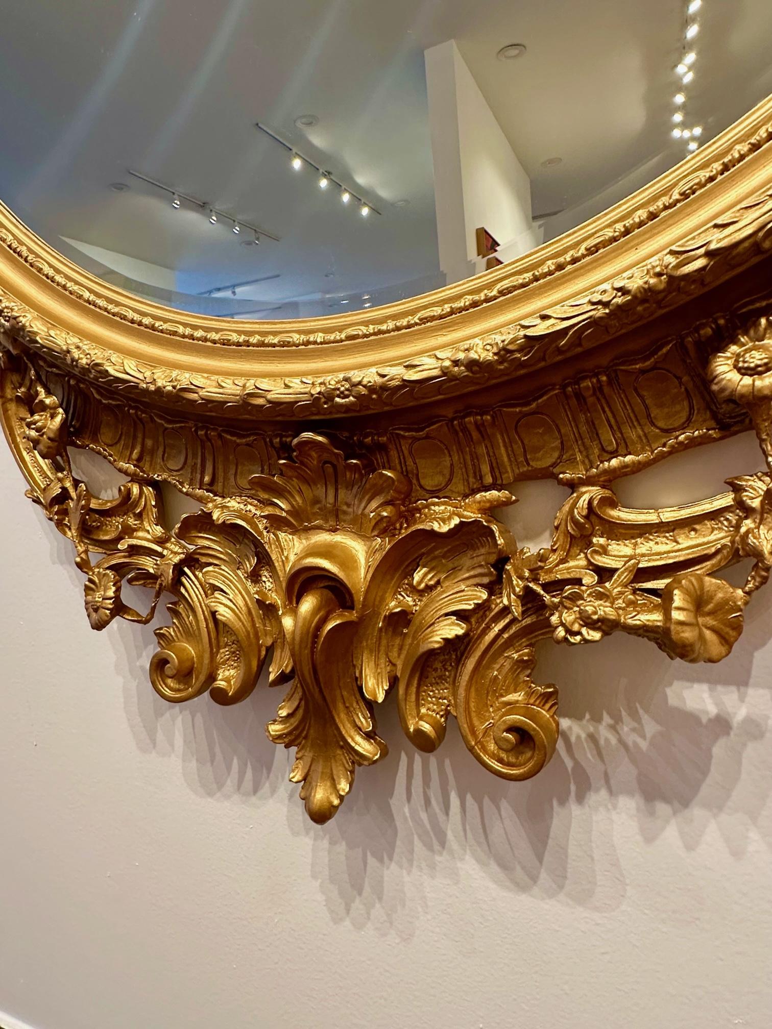 This large oval-shaped mirror is a rare find in all of its grandeur. The shear size is of this mirror is something to behold and appreciate as the ornate carvings and workings of the wood are a testament to the artisanal craftsmanship typical of the