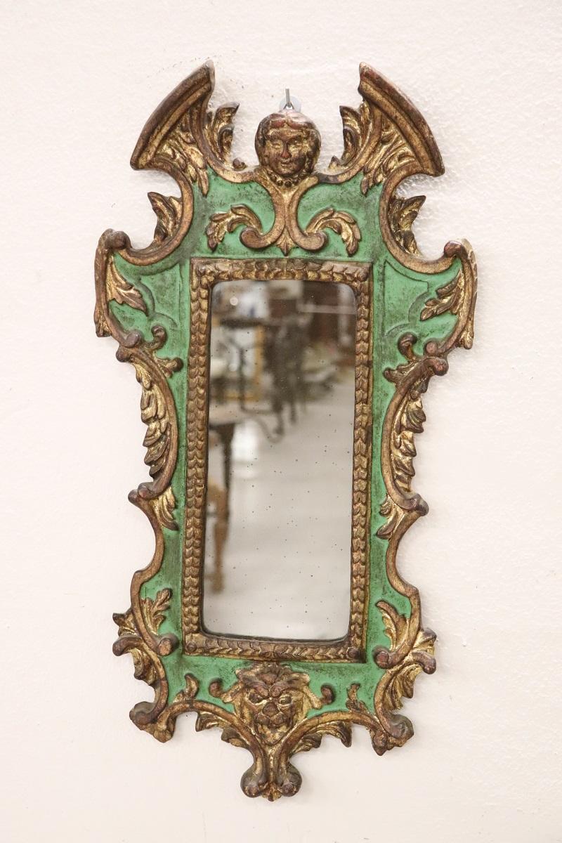 Elegant 20th cetury Italian carved poplar wood wall mirror. The frame is characterized by an elaborate decoration with classic gothic taste. The wood is lacquered in green tones with elegant golden decorations, note the heads carved into the wood.