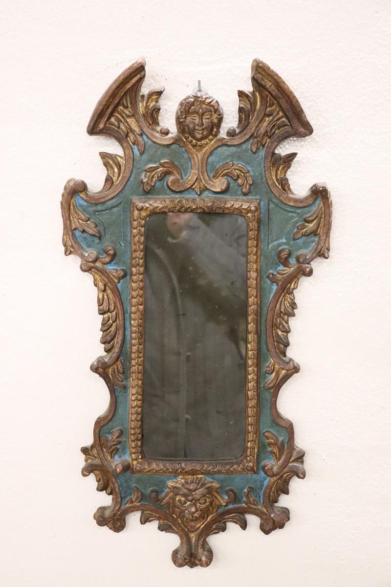 Elegant 20th cetury Italian carved poplar wood wall mirror. The frame is characterized by an elaborate decoration with classic gothic taste. The wood is lacquered in blue tones with elegant golden decorations, note the heads carved into the wood.
