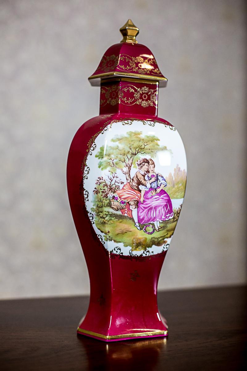 We present you this big vase with a lid.
The item was manufactured in the 1980s, in Limoges, France.
The vase is claret; has gildings.
On one side of the belly, there is a genre scene on an oval, white background.

Measures: Height with lid: 41