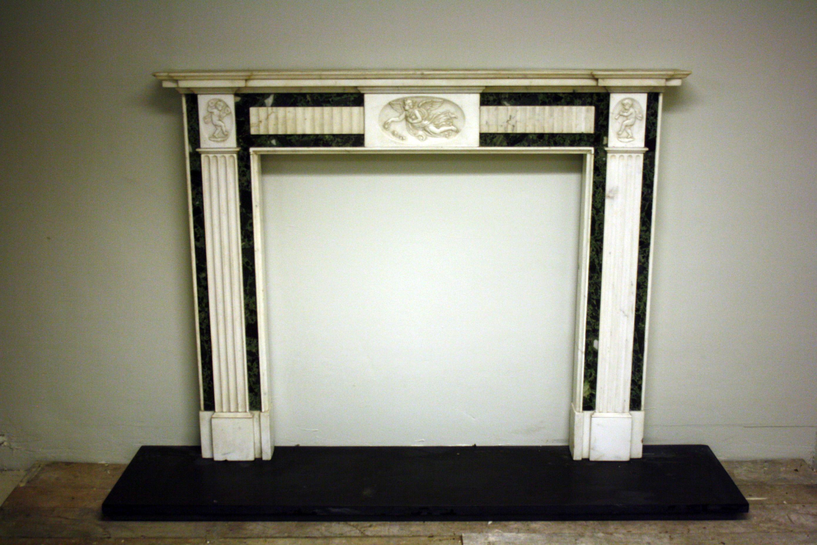 Early 20th century green and white marble fireplace, centre frieze tablet is decorated with carved angel and corner blocks with dancing Putti.

Opening size 94 cm W x 94 cm H.