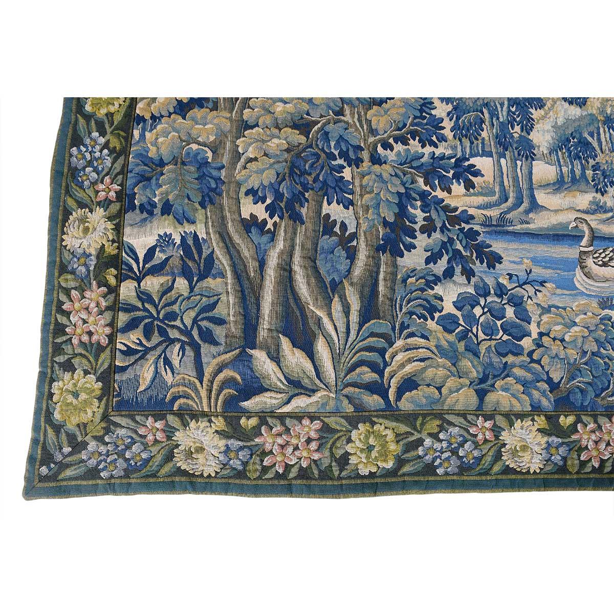 A tapestry by Jaquar in Halluin in the style of a 17th Century Aubusson. The landscape subject features rivers and ducks set among trees all enclosed in a colorful floral border. The label on the back identifies the maker and the style. In very good