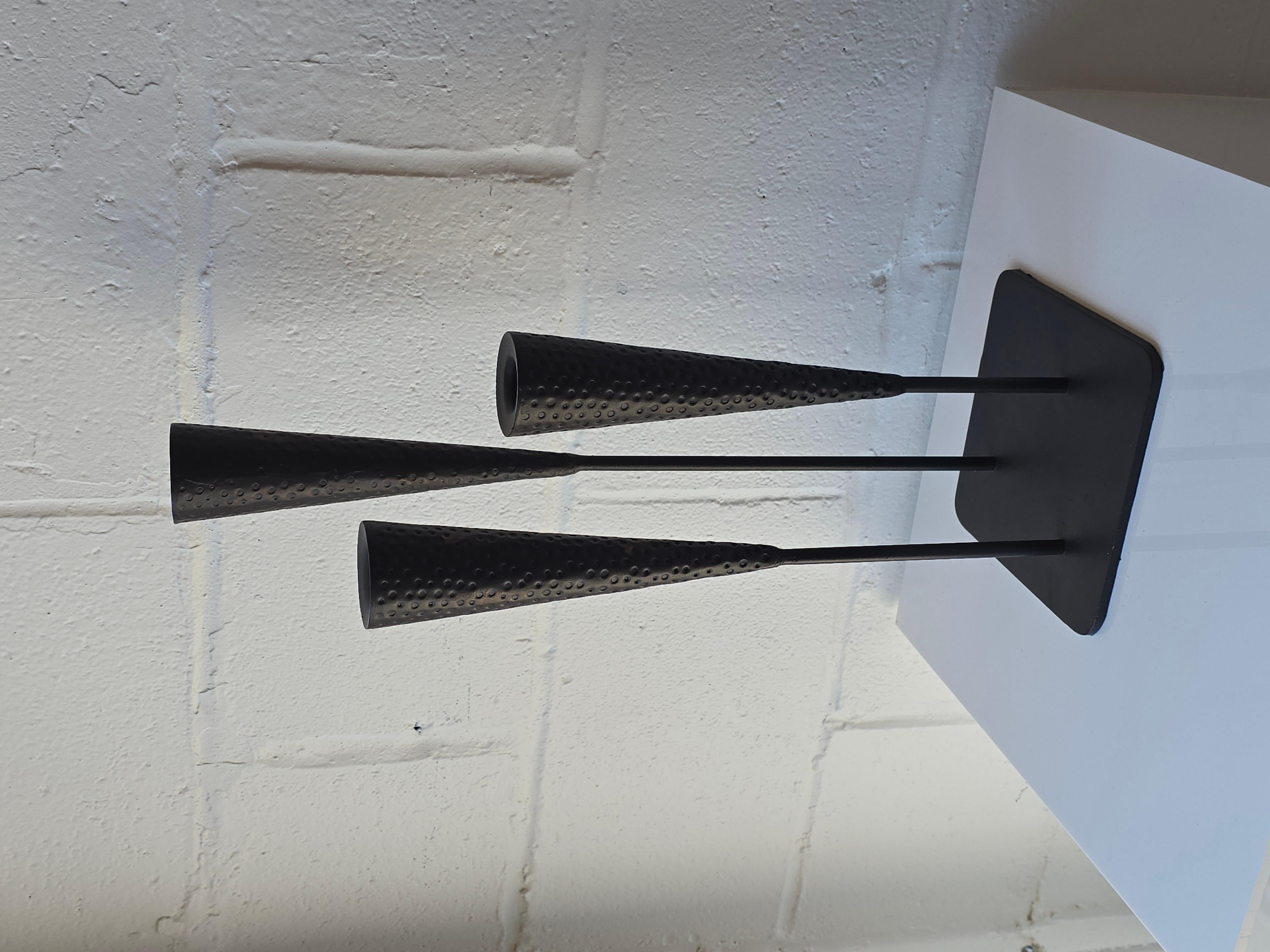 Gorgeous iron candelabra in the style of Harry Bertoia. This candelabra has three rods that are connected to the square base. The three rods each feature a conical semi closed top to place candles in. The conical top has a hammered texture. Its a