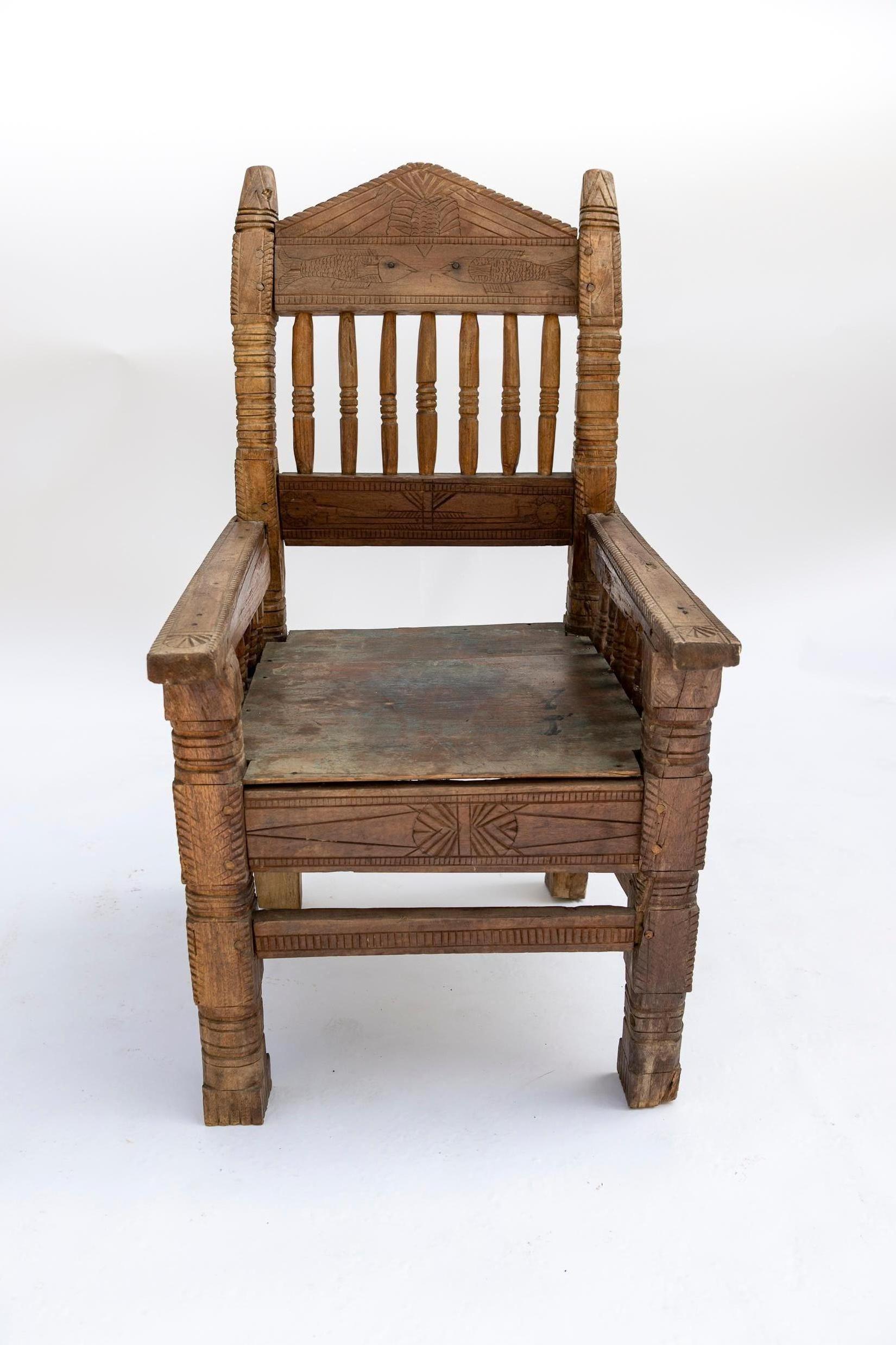 A striking hand-carved wooden chair from Bhutan, dating to the 20th century. This distinctive piece showcases traditional Bhutanese craftsmanship, with intricate geometric and symbolic carvings throughout. The backrest, arms, and seat feature finely