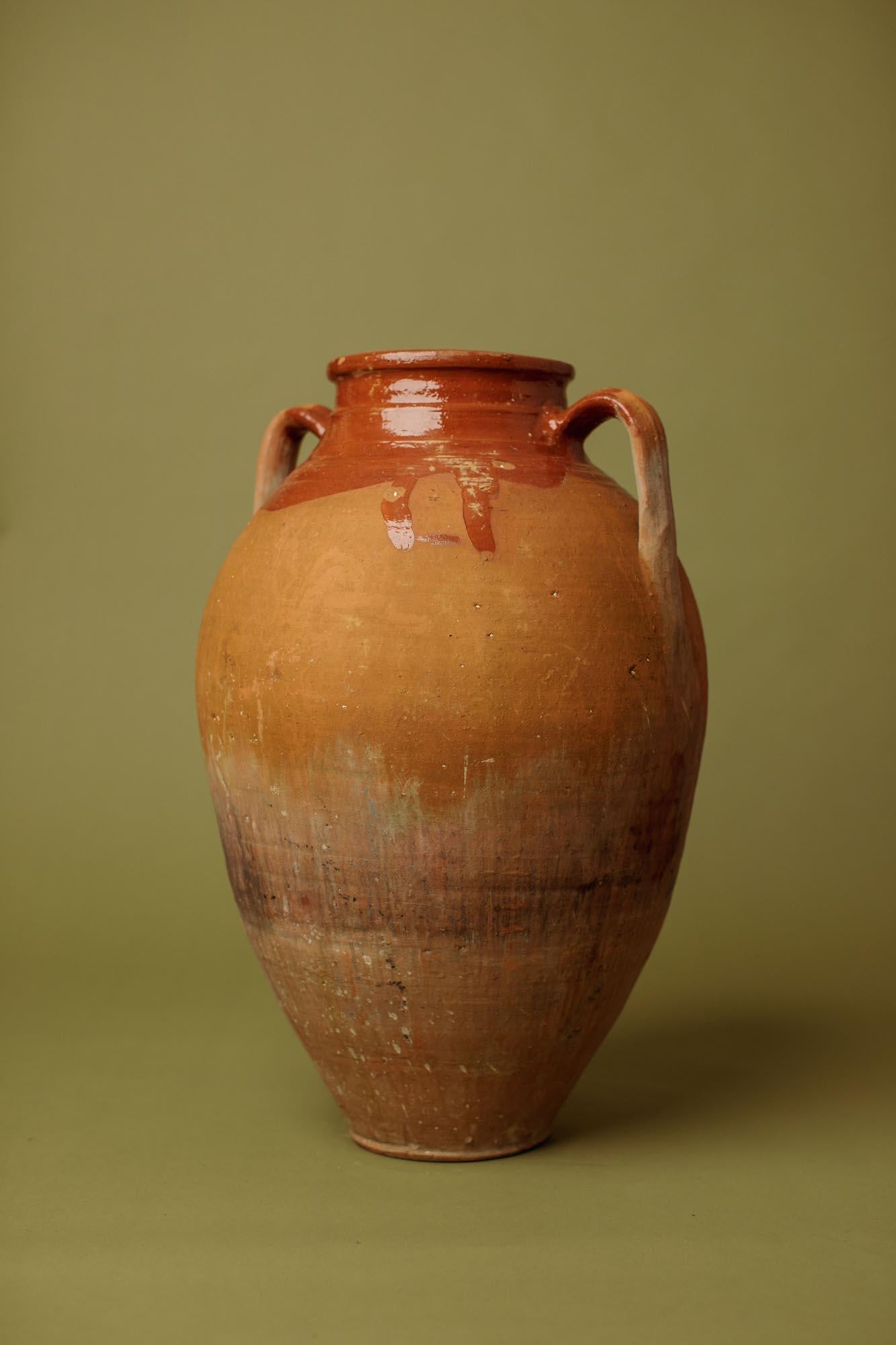 Questa giara in terracotta cotta a mano del XX secolo proviene dall'Anatolia occidentale, dove veniva tradizionalmente utilizzata per conservare olio, olive o cereali. La sua caratteristica superficie bicolore cattura l'essenza dell'artigianato