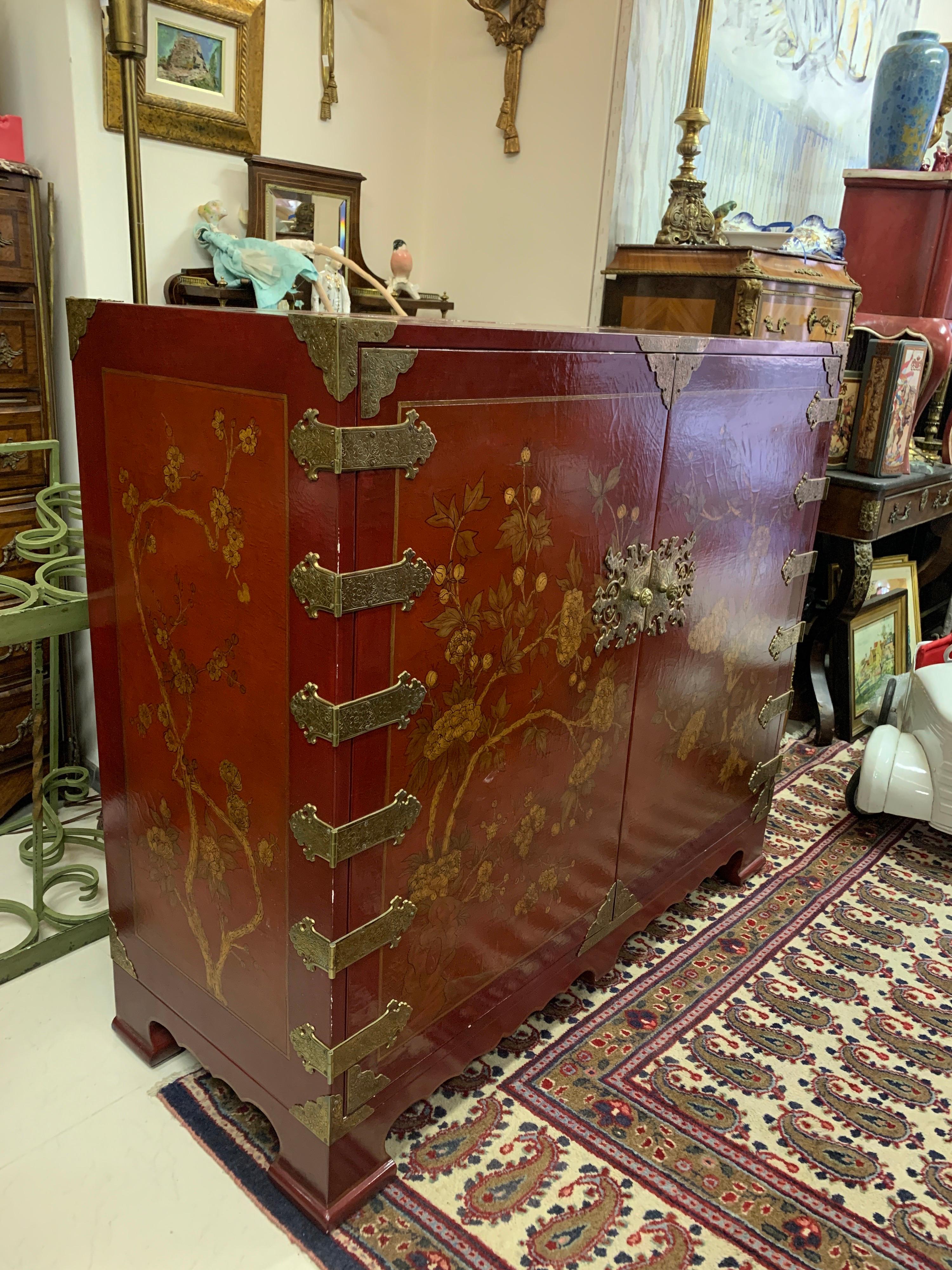 Handbemalter Schrank aus rot lackiertem Holz, verziert mit Blumen und Metallbeschlägen. Im Inneren ist ein Fernsehgerät installiert. 
China
20. Jahrhundert.