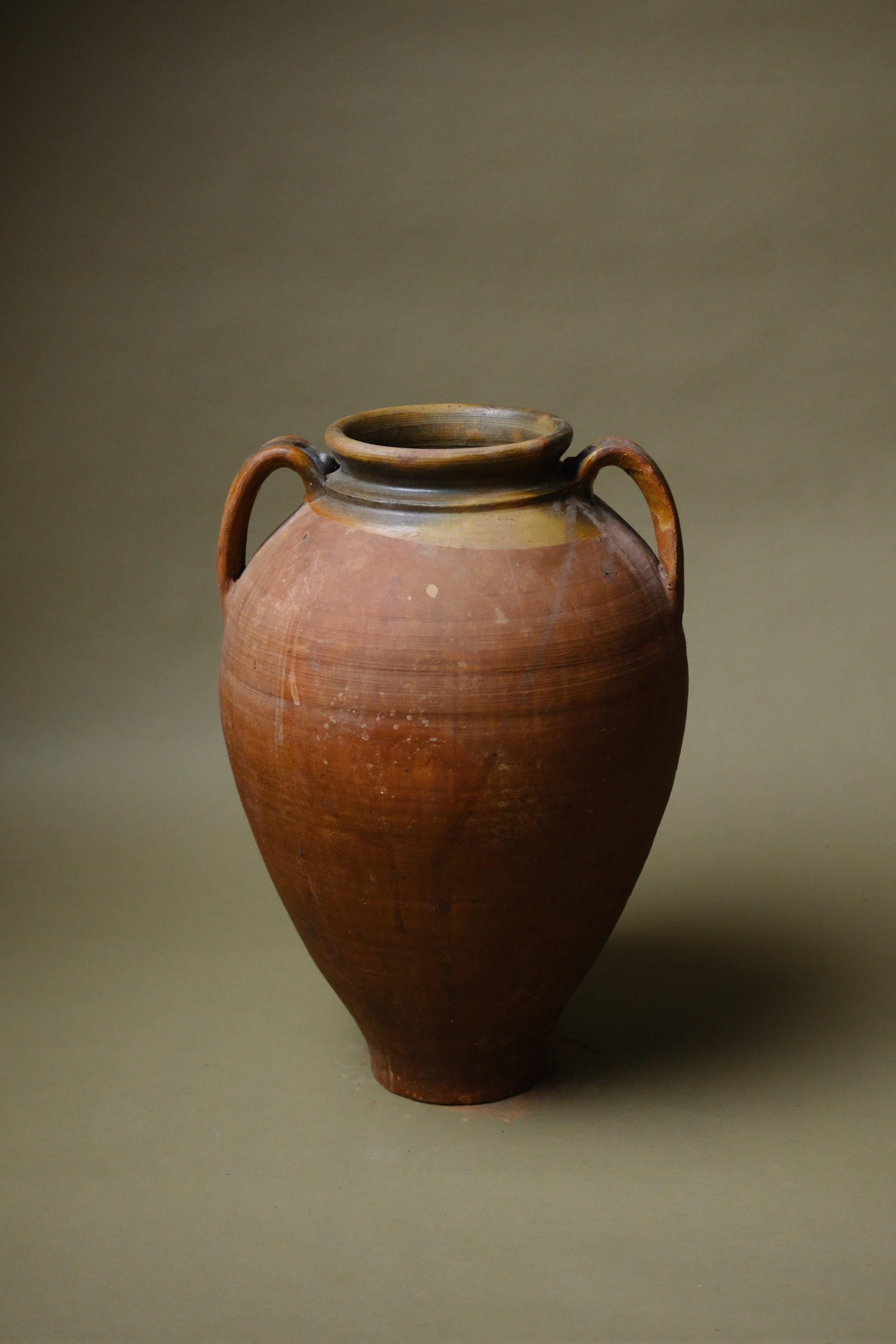 Questa giara turca in terracotta emana un'autenticità senza tempo grazie alla sua superficie liscia, ai doppi manici e al sorprendente bordo smaltato. Realizzato a mano in Anatolia, riflette le abili tradizioni della regione. Le ricche e calde