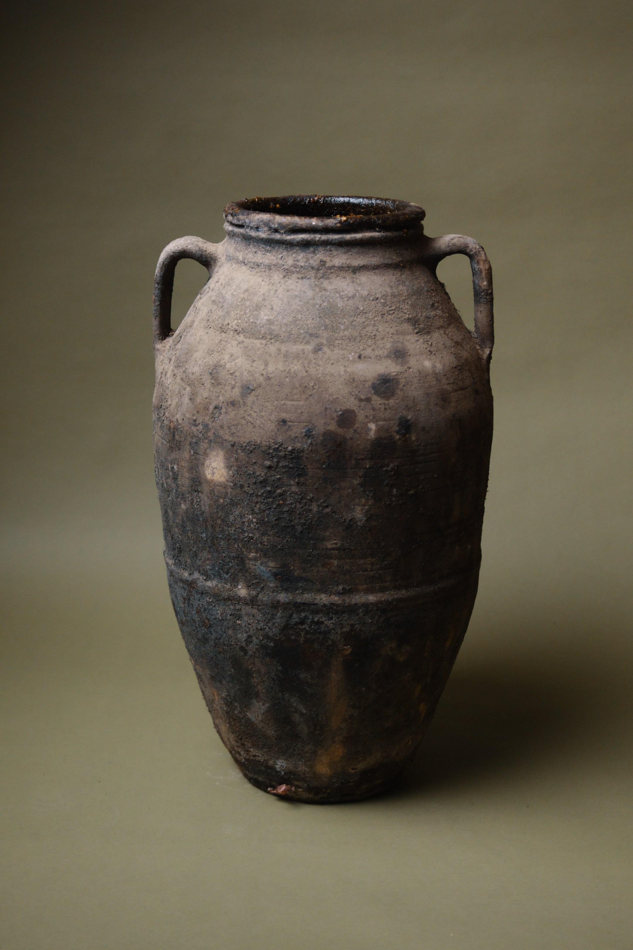 Un'anfora turca davvero affascinante, questo pezzo incarna l'autentica maestria della ceramica anatolica. Proveniente dal ricco patrimonio culturale della Turchia, questa anfora annerita veniva tradizionalmente utilizzata per conservare oli, miele o