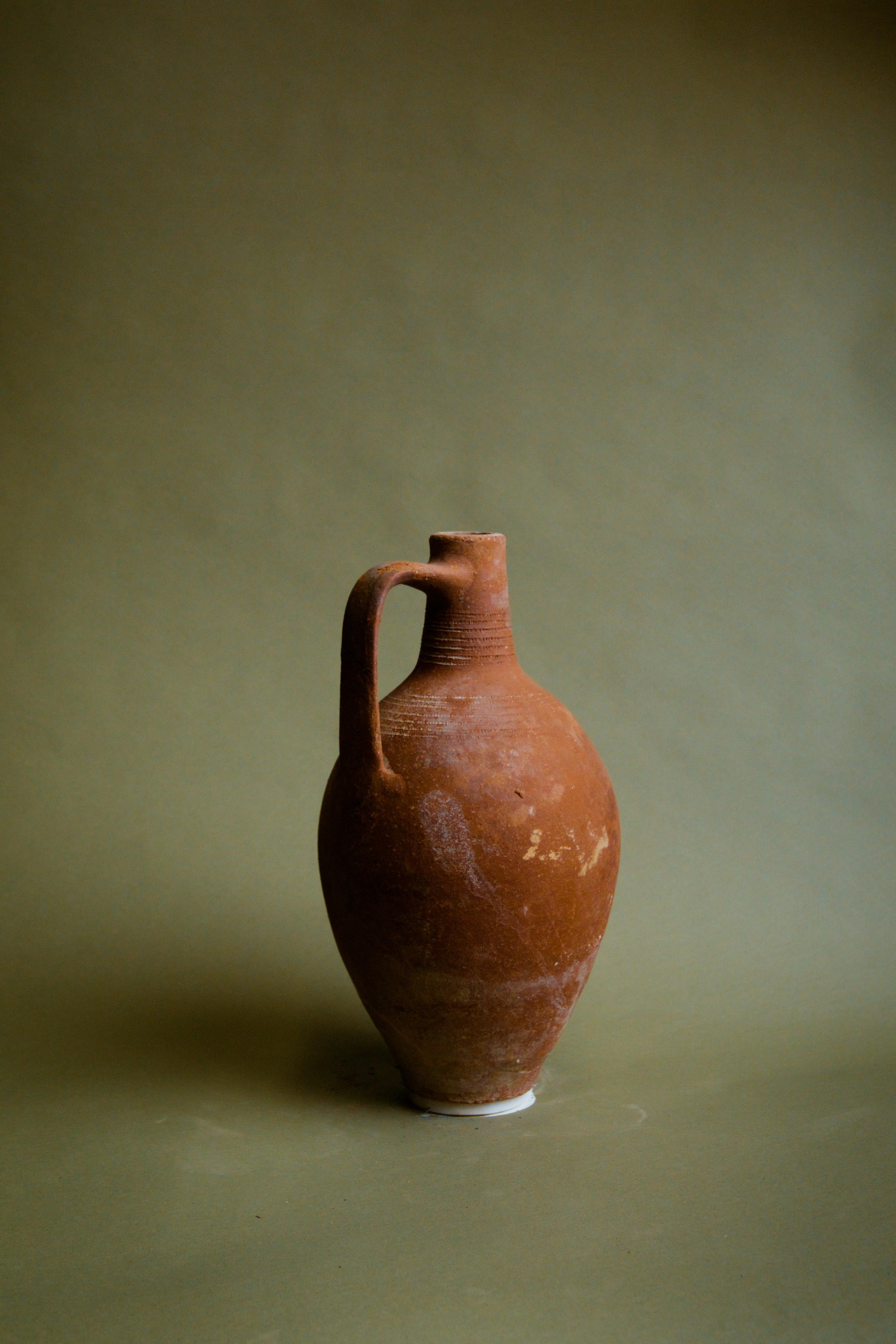 Questa brocca anatolica d'epoca dal manico sottile del XX secolo è uno splendido vaso d'epoca in argilla che cattura l'essenza dell'artigianato turco. Realizzata originariamente in Anatolia, questa brocca è caratterizzata da un manico elegante e