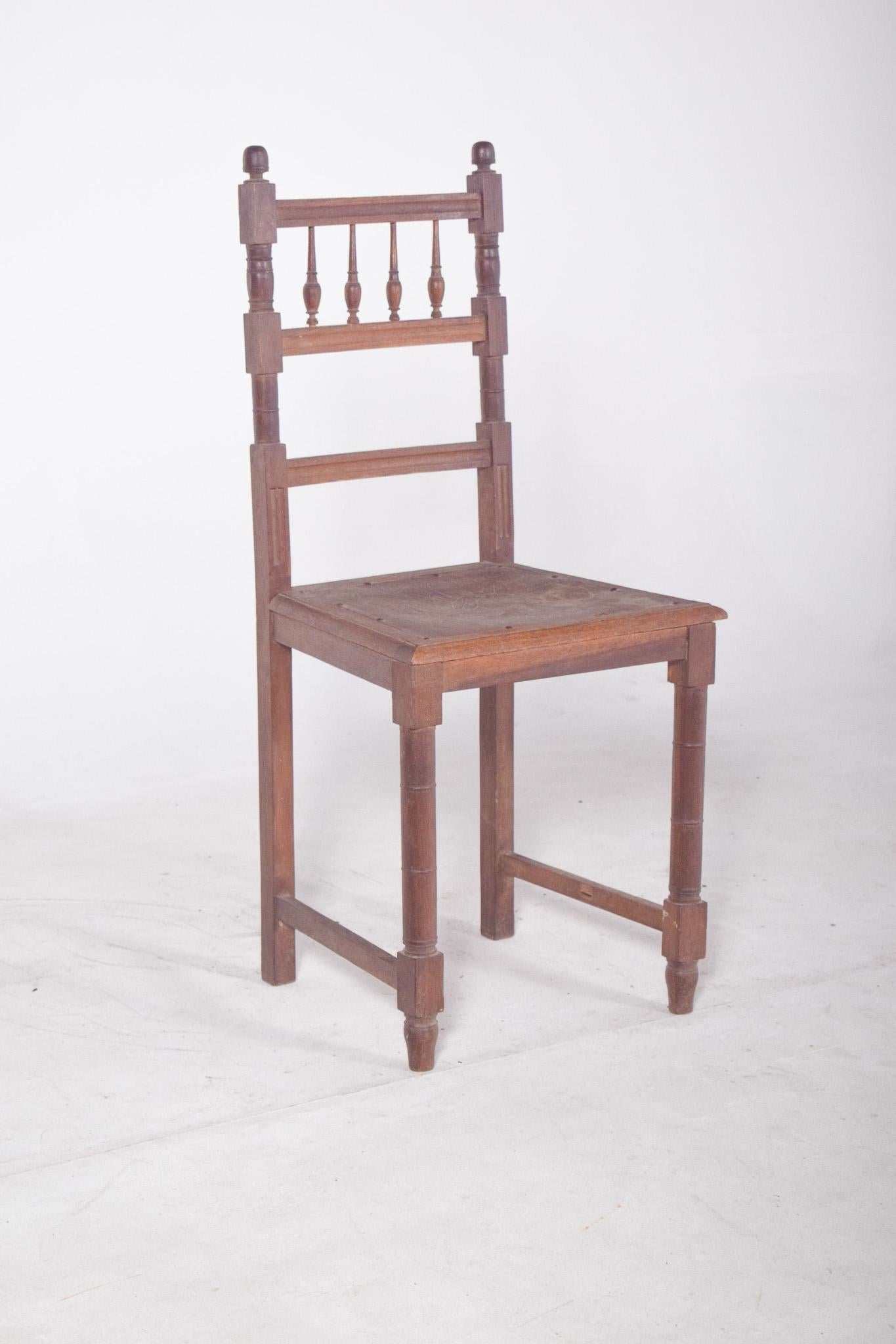 High-backed chair with engraved seat. The backrest is decorated with small turned balusters and side rods topped with rounded pins that emphasise its classic, handcrafted character. The structure is made up of straight, sturdy shapes, with