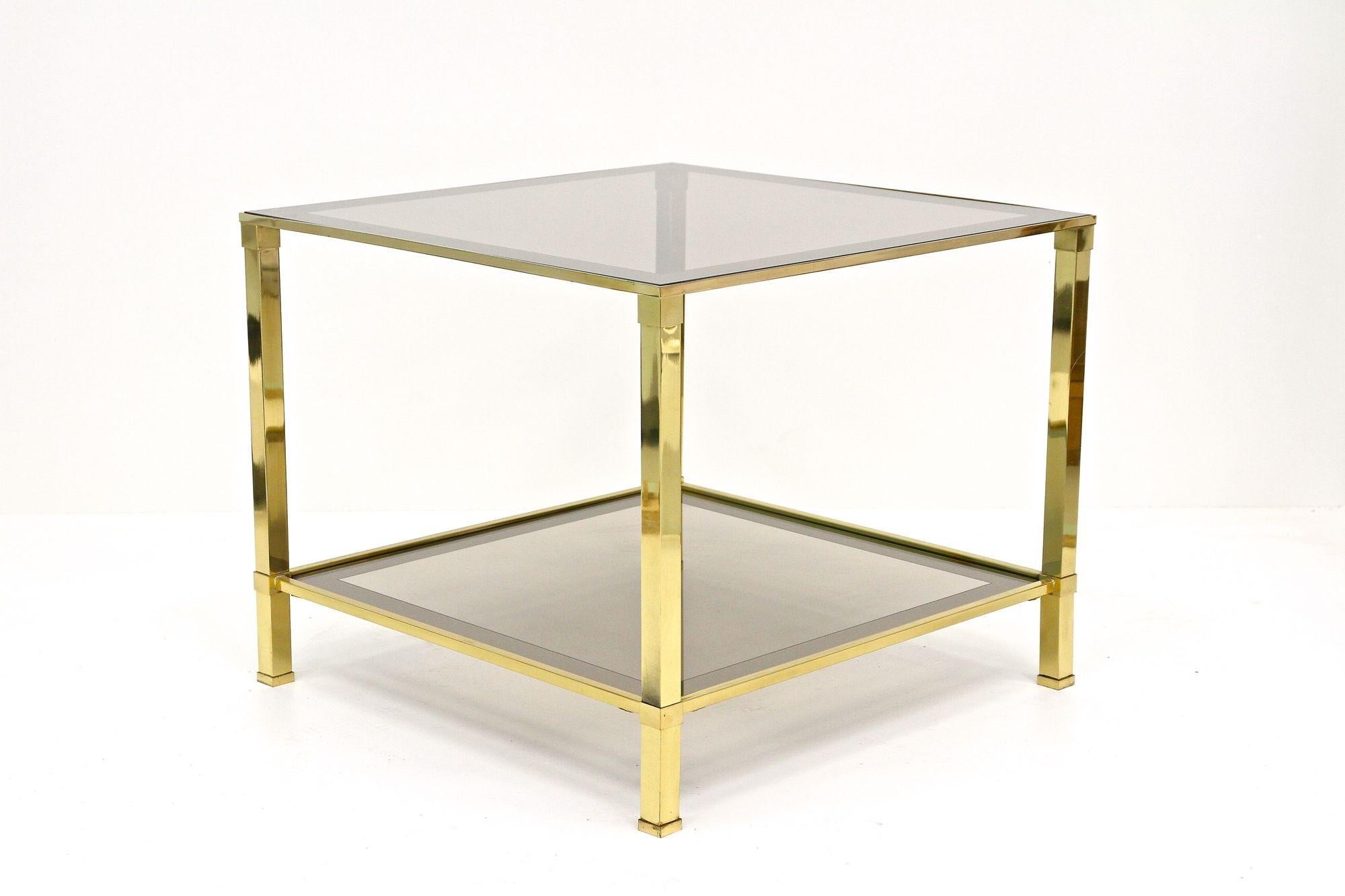 Jolie table d'appoint décorative en laiton de la fin du milieu du siècle dernier, datant d'environ 1970. Cette table d'appoint à deux niveaux de style Hollywood Regency est dotée d'un cadre en laiton doré et de deux plateaux en verre fumé avec des