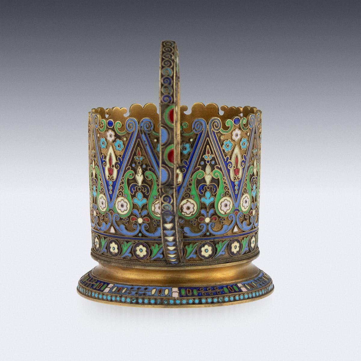 Antique early 20th century imperial Russian solid silver-gilt and cloisonné enamel tea glass holder, circular with upright scroll handle, shaped top rim and spreading foot, body profusely decorated with floral motifs in vary-colored cloisonné enamel