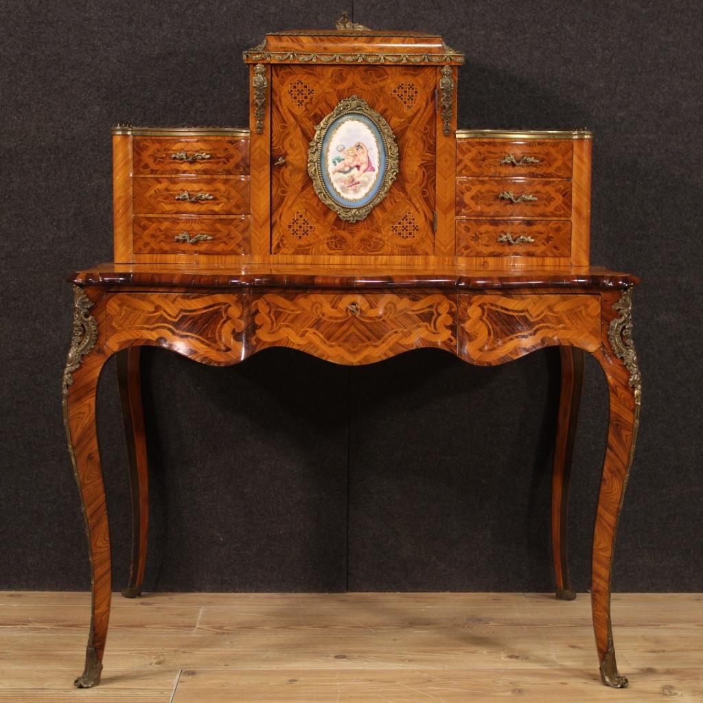 French writing desk from the mid-20th century. Furniture richly inlaid in walnut, rosewood, palisander, kingwood, ebonized wood and fruitwood. Writing desk with shelf adorned with gilded and chiseled bronze and brass with a porcelain plaque