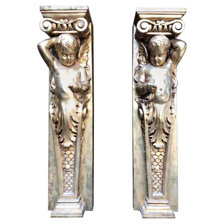 A pair of 20th century gold gilded ionic columns with winged cherubs and fish scaled plinths. These classical columns are from the three orders beginning with the Doric, then the Ionic and ending with the Corinthian. Ionic columns always have a