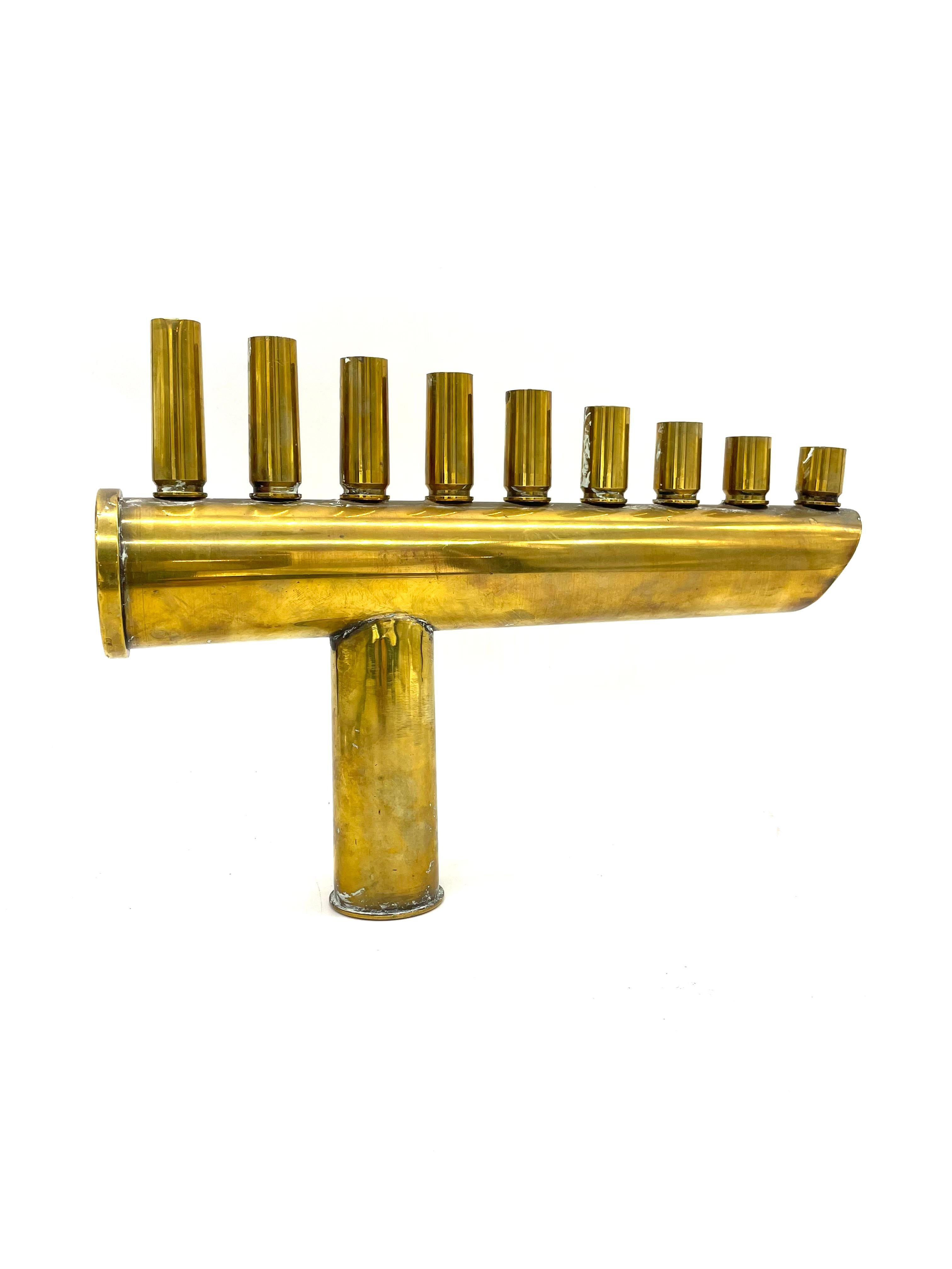 A brass Hanukkah lamp made by Israeli Defense soldiers features nine bullet and shell cartridges in form of candleholders. The bullet cartridges are screwed onto a shell cartridge, itself supported on two additional bullet cartridges. Candleholders