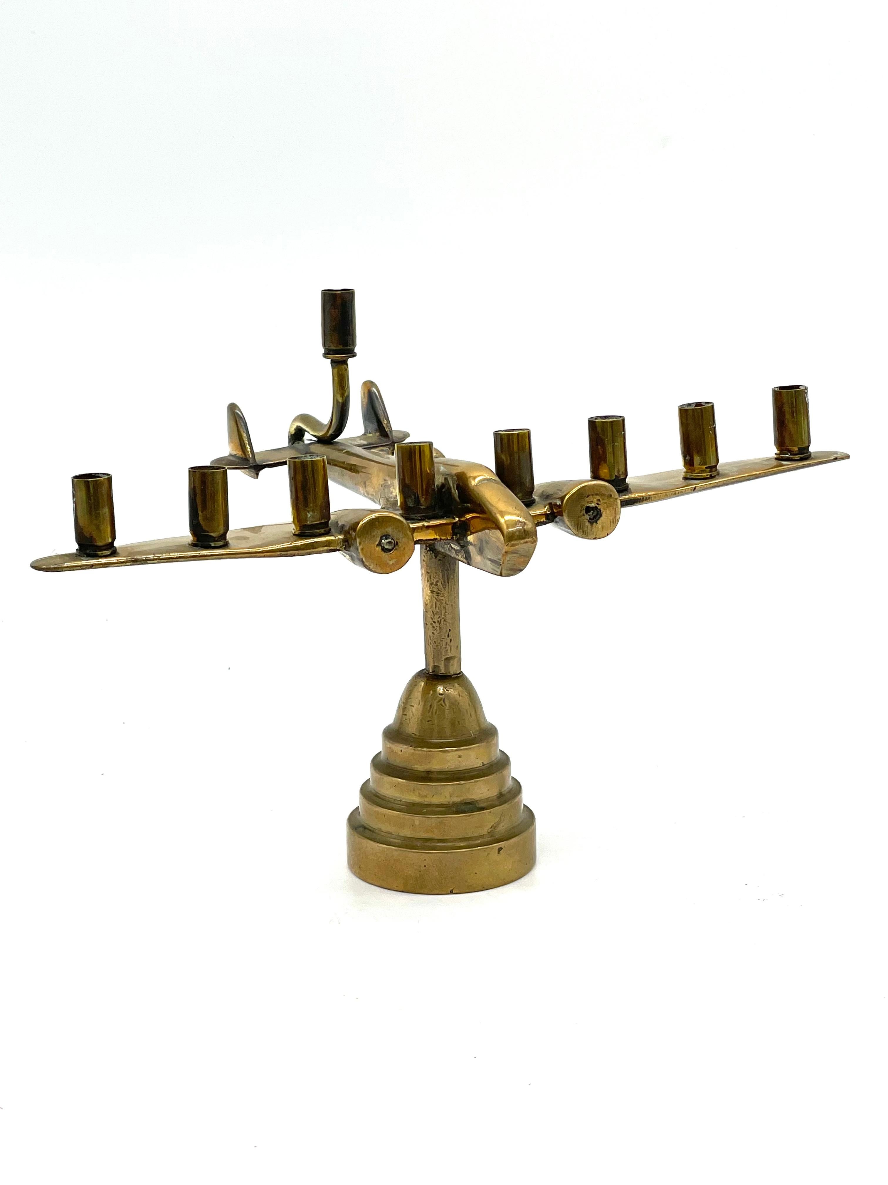 A brass Hanukkah lamp made by Israeli Defense soldiers features nine bullet and shell cartridges in the form of candleholders. The bullet cartridges are screwed into shell cartridges that are supported by a horizontal surface mimicking the shape of