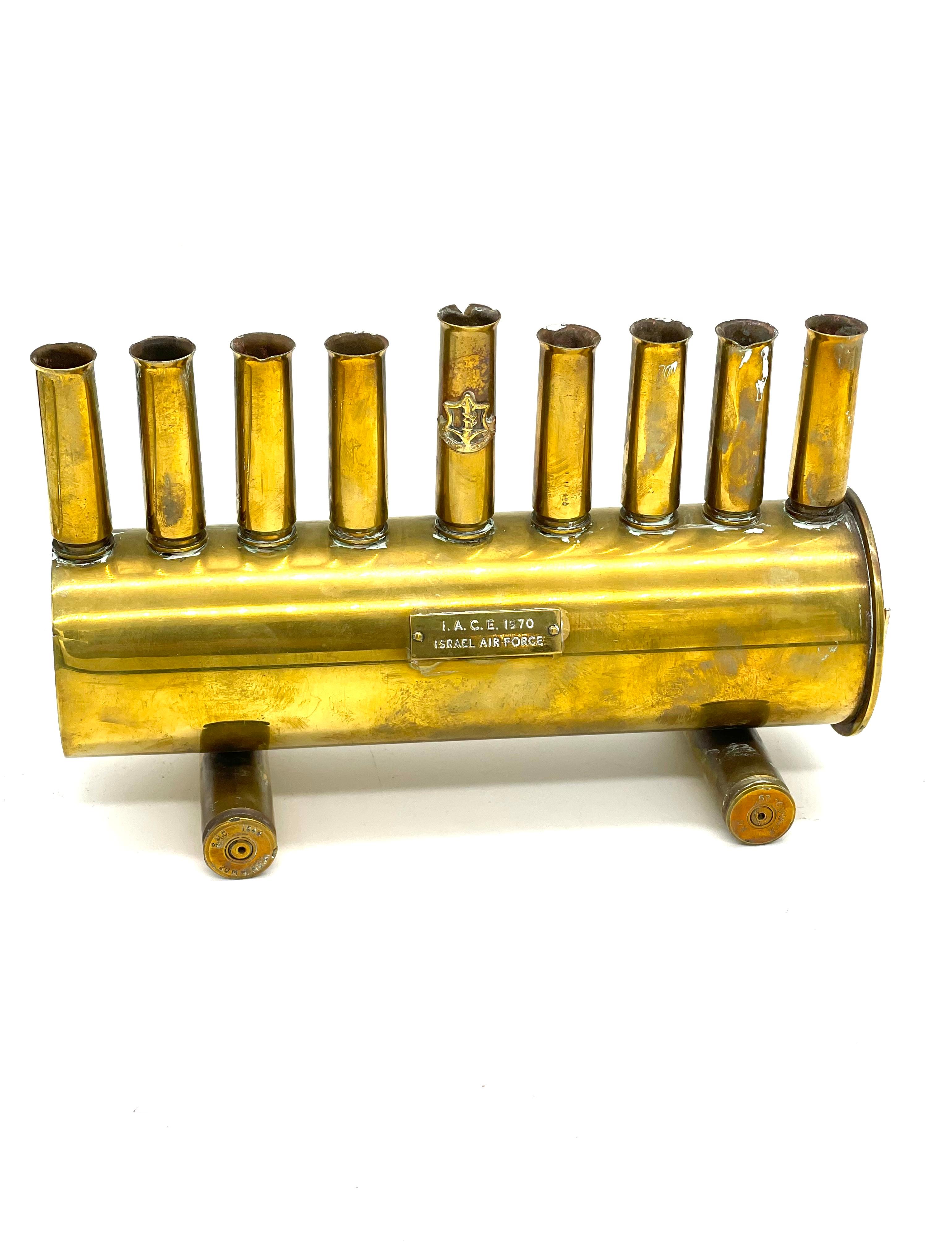 A brass hanukkah lamp made by Israeli Defense soldiers features nine bullet and shell cartridges in the form of candleholders. The bullet cartridges are screwed into a 75-mm shell cartridge, itself supported on two additional bullet cartridges.