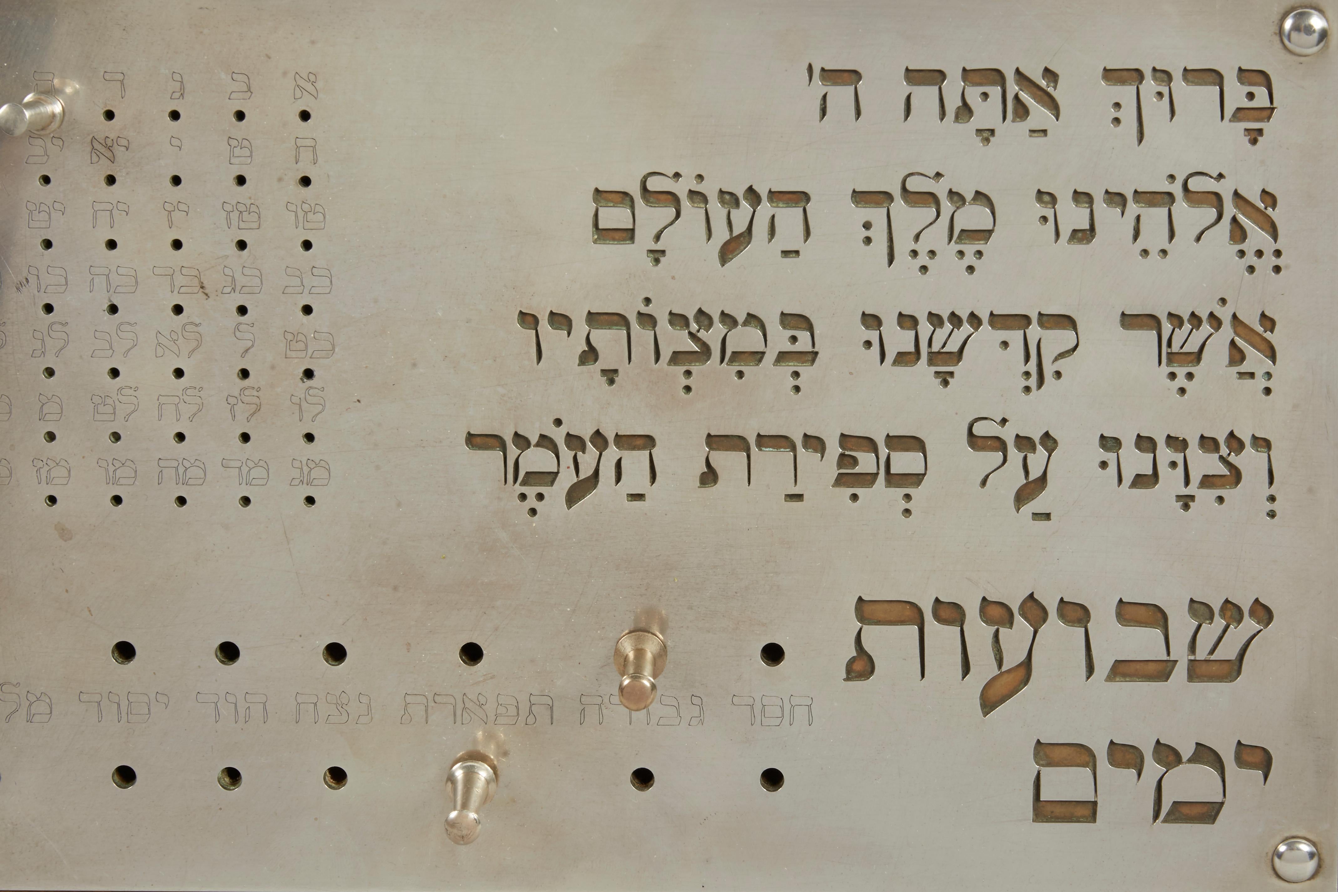 Omer counter, sterling silver, brass, and wood, Jerusalem, Israel, circa 1985.
Silver Omer counter over brass background on wood base with silver pins for counting.
Cut out Hebrew features the blessing for counting the Omer: 