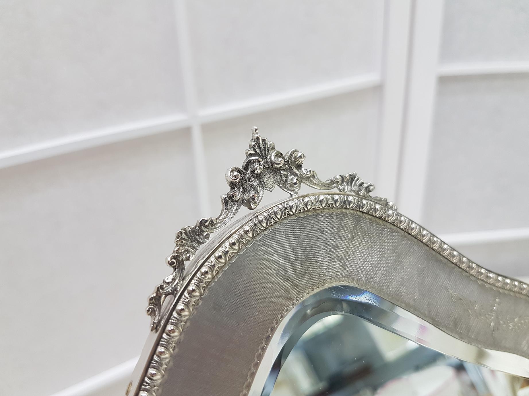 Solid shaped silver table mirror engraved with knurling and with flowers. The edge of the mirror is welded and decorated with a cord. The feet are worked in fusion and chiseled as well as the upper crest.
The back, completely restored, is in