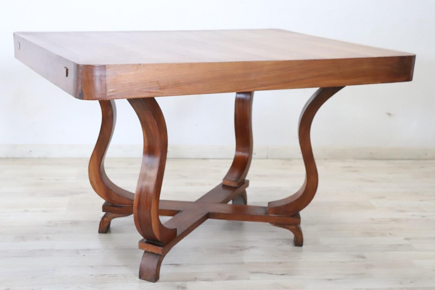 Delicious Italian Art Deco table 1930s. Made of fine veneered walnut. On the sides two supports may contain a small top to extend the table, but the tops have been lost. The four wavy legs that support the top are beautiful. Perfect table for a