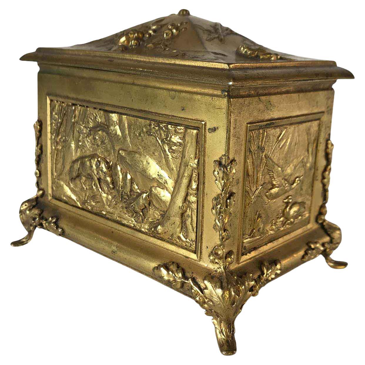 Jewelry box with animals in gilt metal, rectangular shape resting on four feet featuring embossed acorns and oak leaves, decorated on each side with different animals within squared frames. The front is finely repoussé with wild boars in the woods;