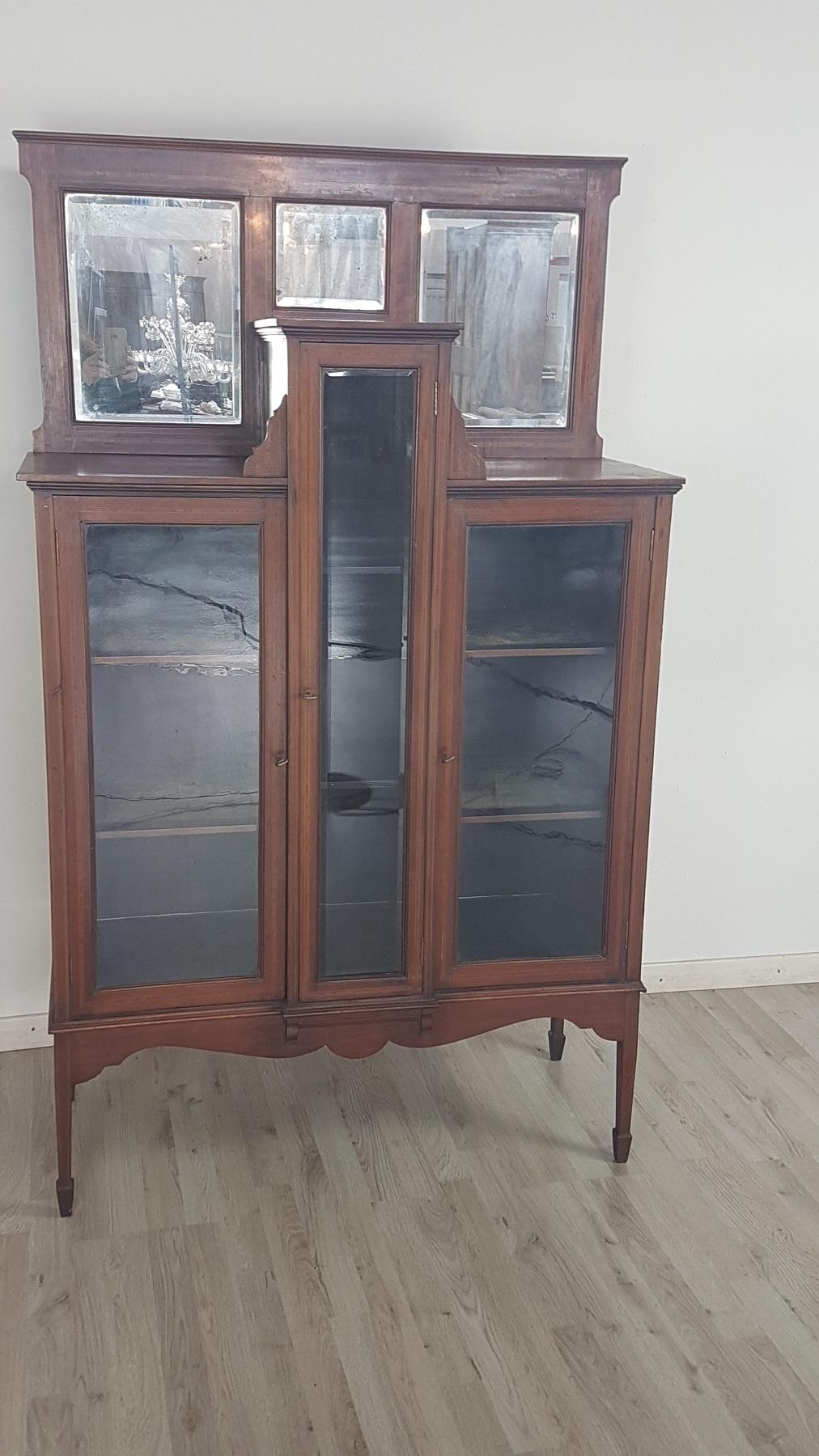 Elegant antique vitrine in walnut veneered with refined inlays and bevelled mirrors. Essential line typical of the early Liberty period of the early 1900s. Good internal capacity. The display case is used but in very good condition to indicate small