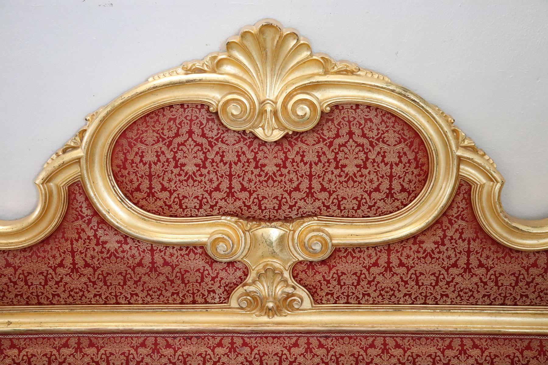 Italian Baroque style bed frame. Rich double bed headboard in carved and gilded wood. Great woodwork with lots of curls and swirls of typical Italian Baroque taste. In the central part a refined red fabric.