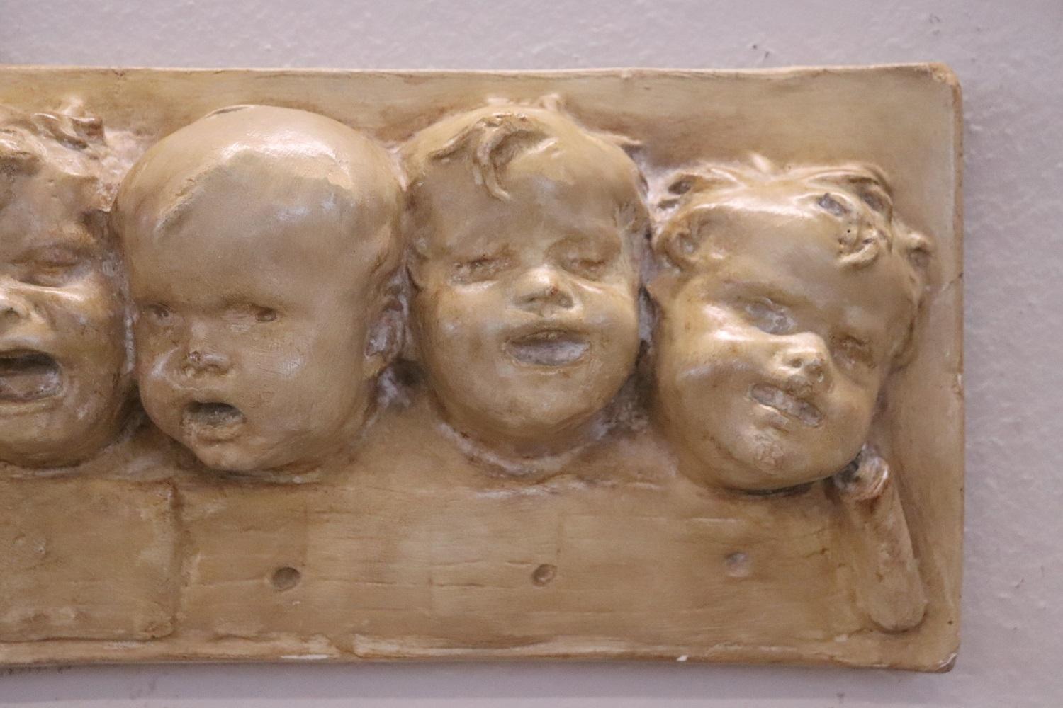 Refined Italian sculpture in plaster. Adorable bas-relief with cherub heads, each one has a different facial expression. The plaster has been painted. Particular piece of furniture in perfect condition.