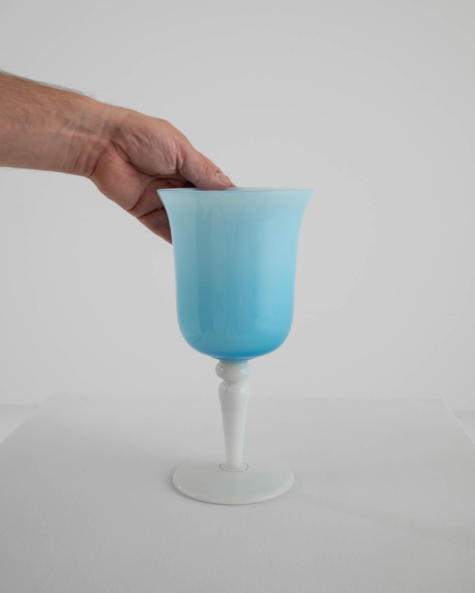 Behold the allure of this 20th Century Italian Blue Glass Goblet, a masterpiece in opaline craftsmanship. The goblet boasts a white base that serves as the perfect pedestal for its enchanting ice blue cup. A subtle gradient, transitioning from a