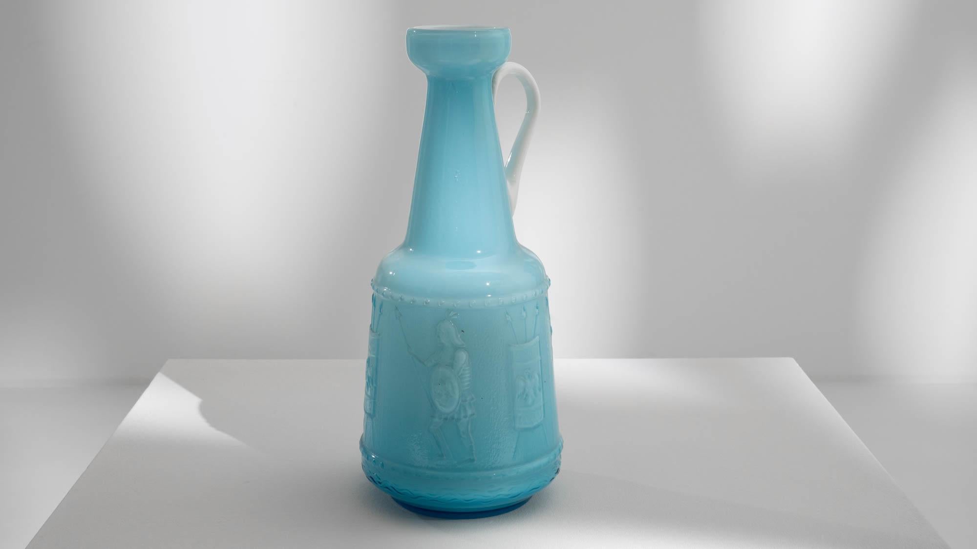 This 20th Century Italian Blue Glass Jug is a captivating piece featuring a Roman warrior preparing for battle. The intricate depiction showcases a figure from the Roman Empire holding a shield and spear, depicting a moment of historical intensity.