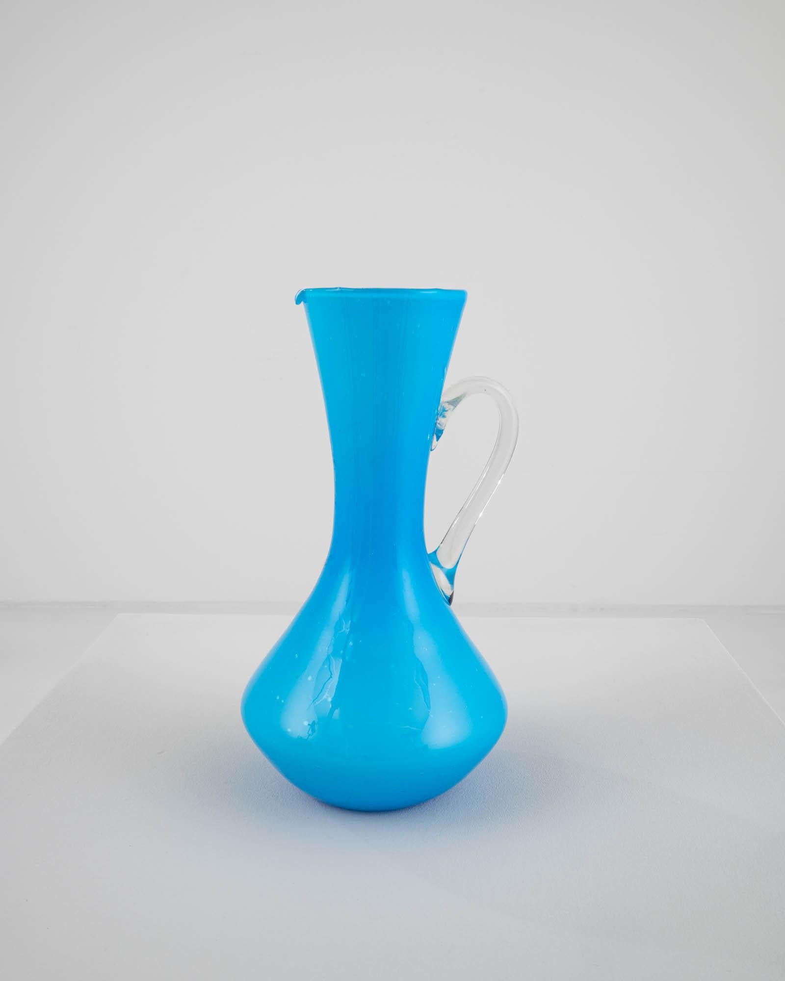 This 20th Century Italian Opaline Medium Blue Glass Jug captivates with its timeless sophistication. The rich, medium blue hue exudes an elegant allure, elevating its aesthetic appeal. With a gracefully contoured form, the jug features a wide base