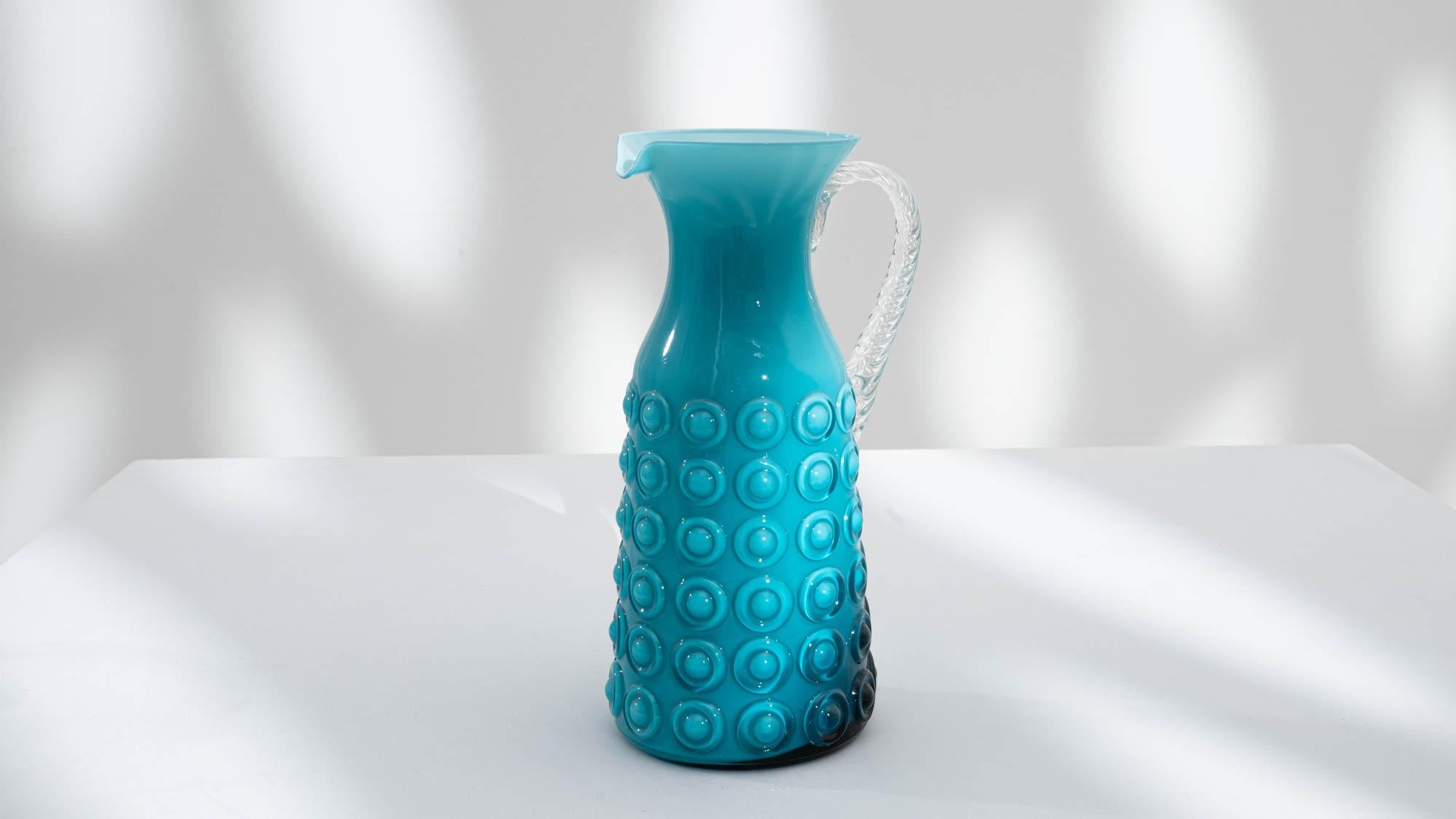 Exemplifying artistic innovation, this 20th-century Italian blue glass jug showcases a captivating 3D bubble design, bathed in a mesmerizing bright blue/green hue. The handle, rendered in textured white glass, adds a tactile element to the jug's