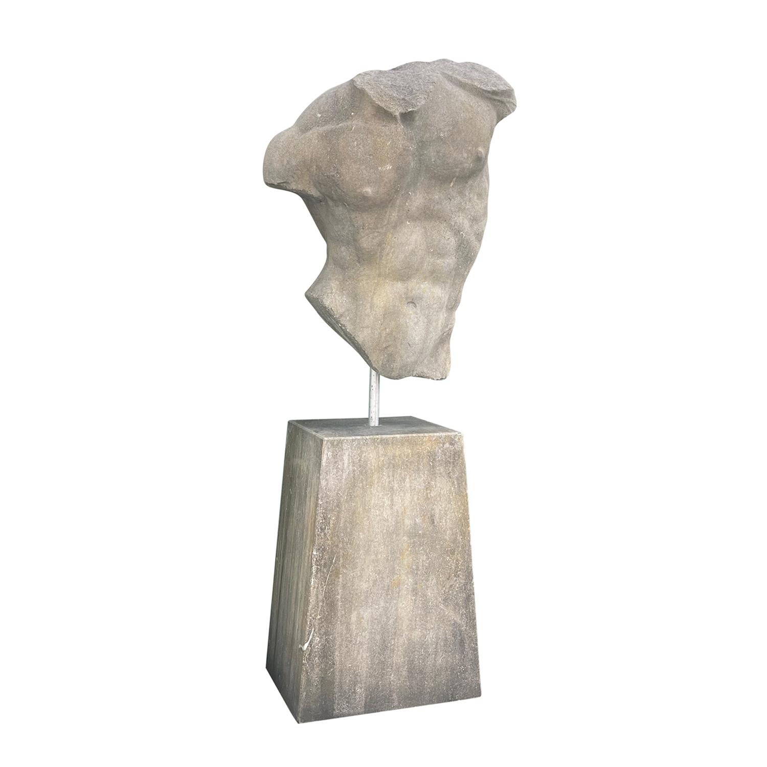 A tall limestone statue of a male torso carved in the Classical style. The details remind of the Italian Renaissance period. The large vintage Italian male torso sculpture is positioned on a trapezoid shaped plinth. Weather patina, wear consistent
