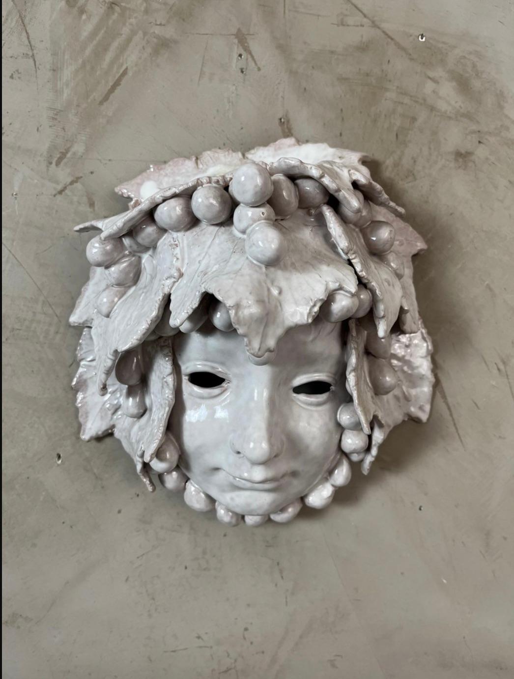 Aggiungi un tocco di poesia e originalità al tuo arredamento con questa affascinante maschera da parete in ceramica ispirata a Bacco, il dio del vino. Realizzato a mano, raffigura un volto sereno e infantile delicatamente incorniciato da foglie