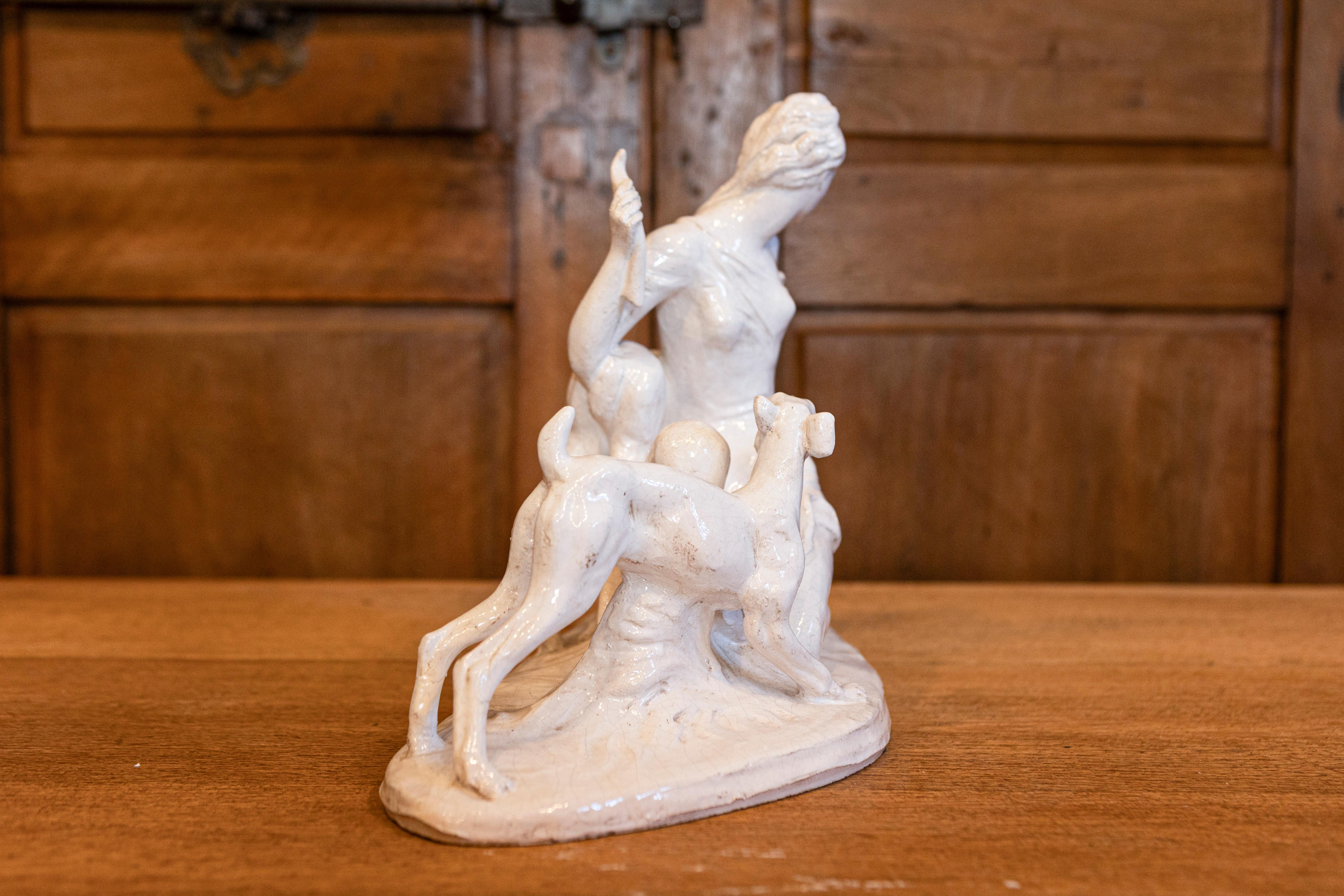 Questa scultura in ceramica italiana del XX secolo raffigura Diana, la dea romana della caccia, in una posa elegante e dinamica. Realizzata con uno smalto bianco lucido, la scultura mostra Diana seduta con grazia in mezzo a due cervi, che