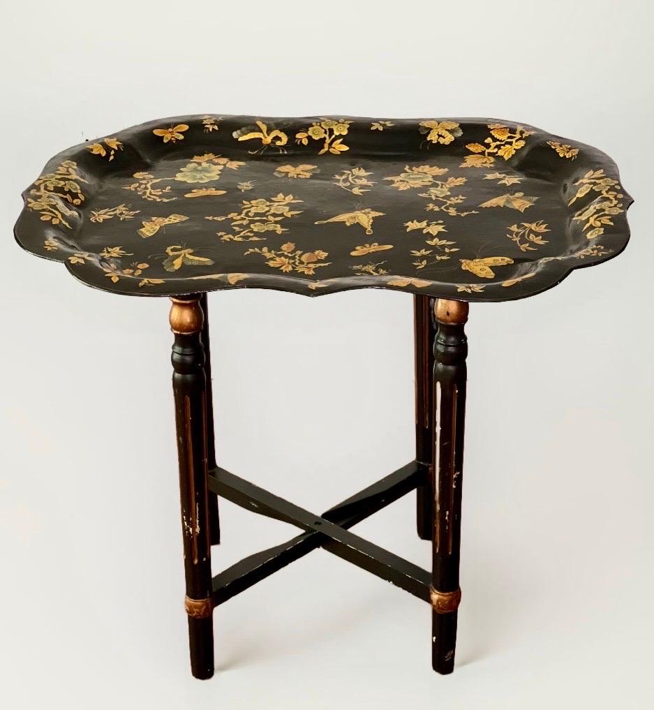Table à plateau en tole laquée noire de style Chinoiserie italienne avec base pliante en bois ébonisé. Il présente un ravissant motif peint à la main avec des papillons et des fleurs dans des tons dorés et des couleurs douces. Les papillons sont