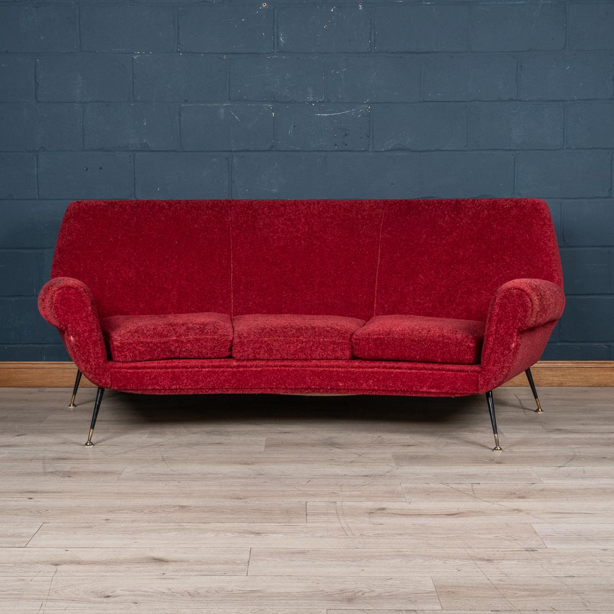 A curved sofa made in Italy in the middle part of the 20th century. The sofa has been upholstered in a sumptuous crimson boucle’ fabric, the striking mid century design with sharp angles, tapered legs finished with brass tips fits so well in any