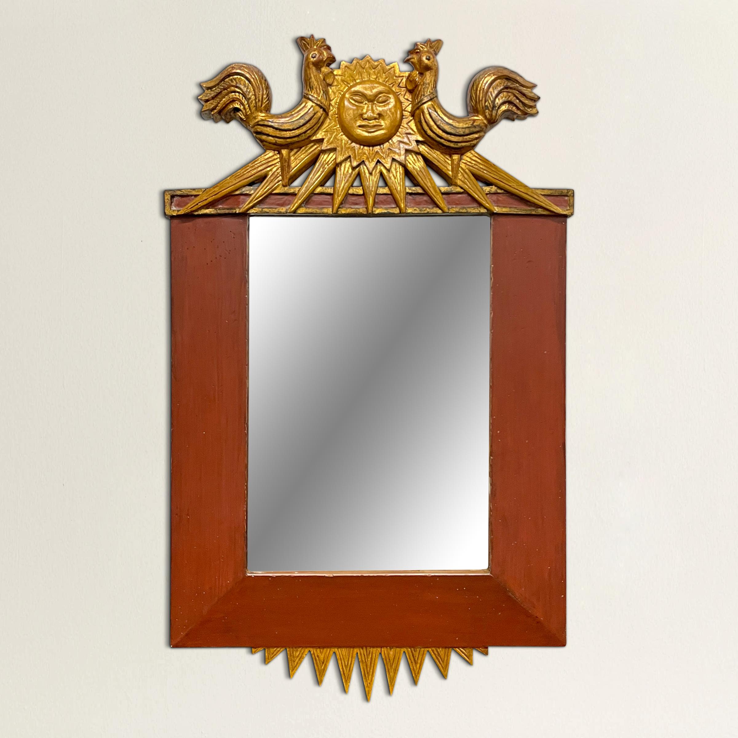 A striking 20th century Italian Empire-style framed mirror with a gilt wood crown depicting two large roosters flanking a gilt sunburst with a face, more gilt wood sun rays at the bottom, and wide beveled brick red painted frame with gilt sides.