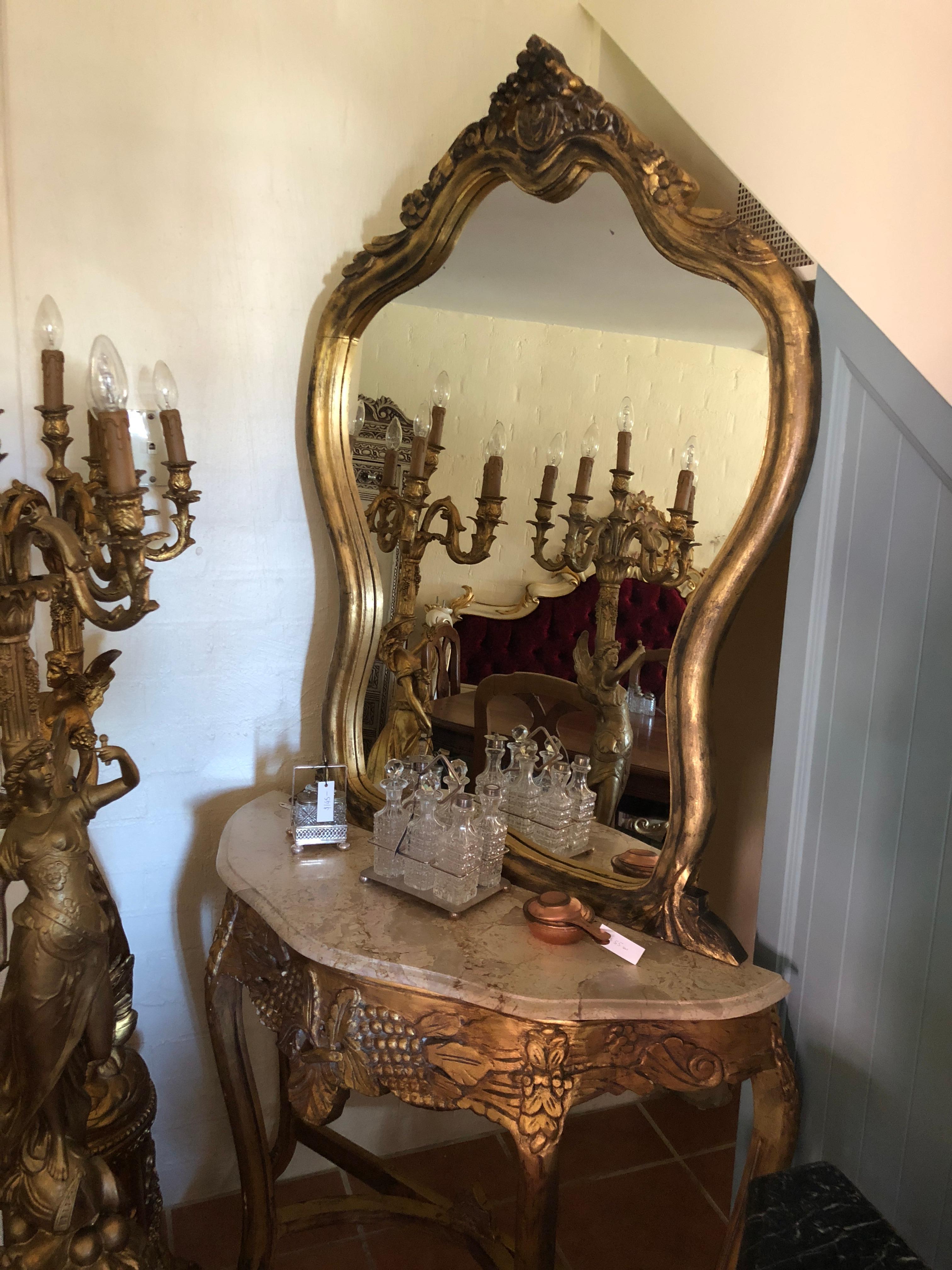 Gilded and adorned with depictions of grape vines, this superb Italian mirrored console would be well suited as a ladies vanity, console or as a mirrored entry hall piece. The elegant shape of the mirror leads down to a creme Italian marble top and