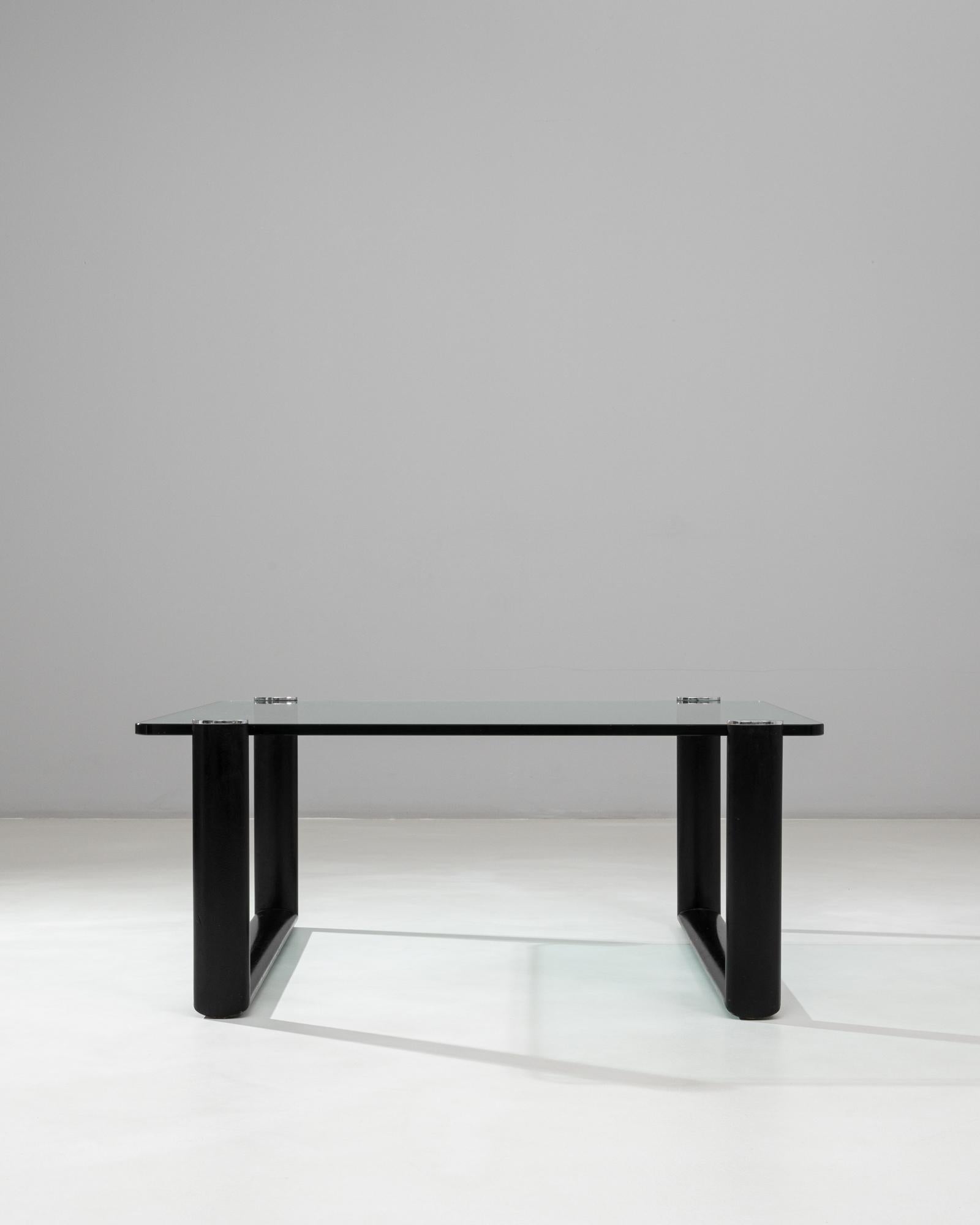Cette table basse en verre italienne du 20e siècle combine des lignes modernes et épurées avec des éléments subtilement sculpturaux. L'épais plateau rectangulaire en verre repose sur un socle en bois distinctif fini dans un noir mat profond, créant
