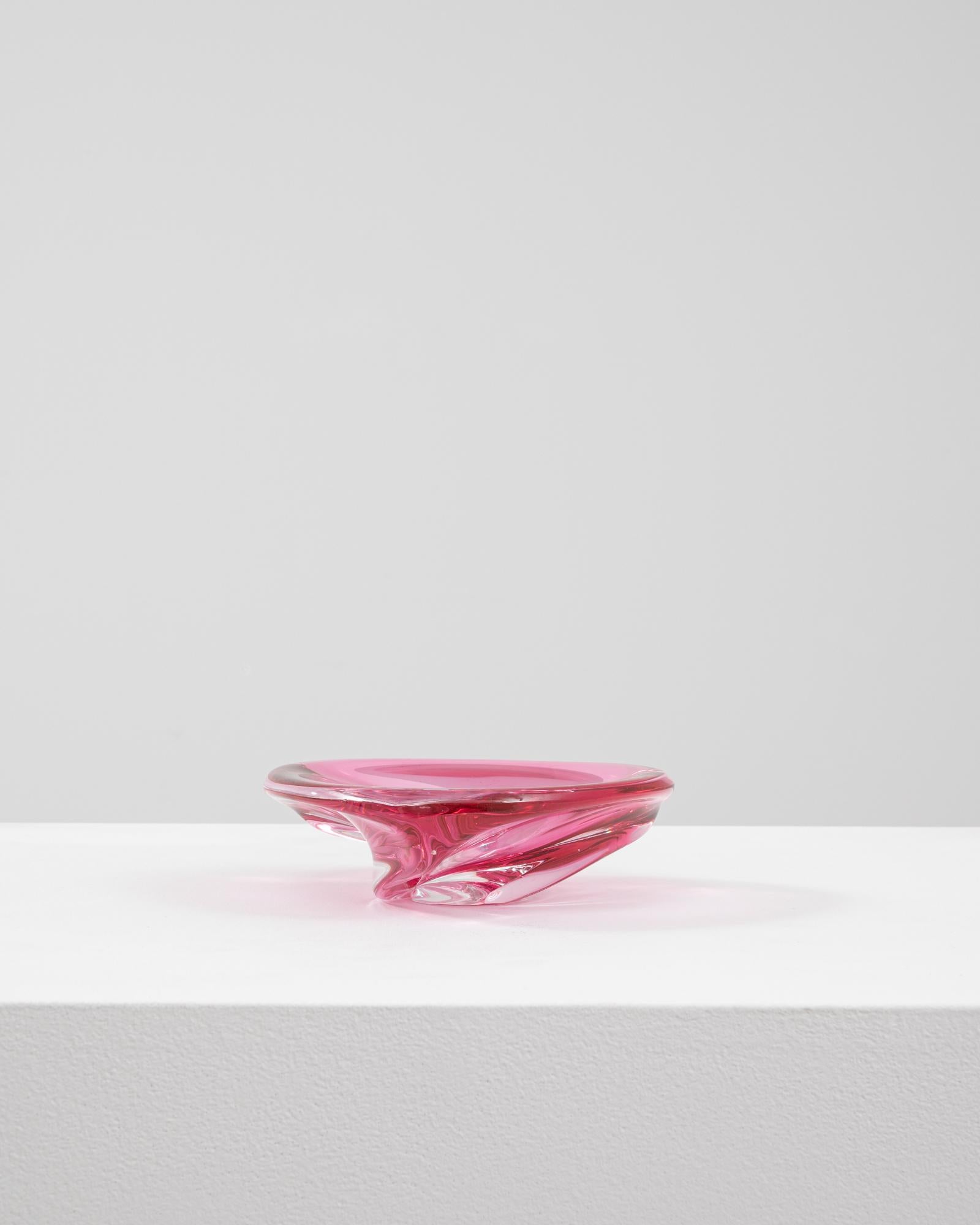 This 20th Century Italian glass plateau is a striking example of mid-century Murano craftsmanship, rendered in a vivid raspberry pink with a clear glass base. Its low, rounded form is accentuated by smooth contours and gently twisted sides, creating