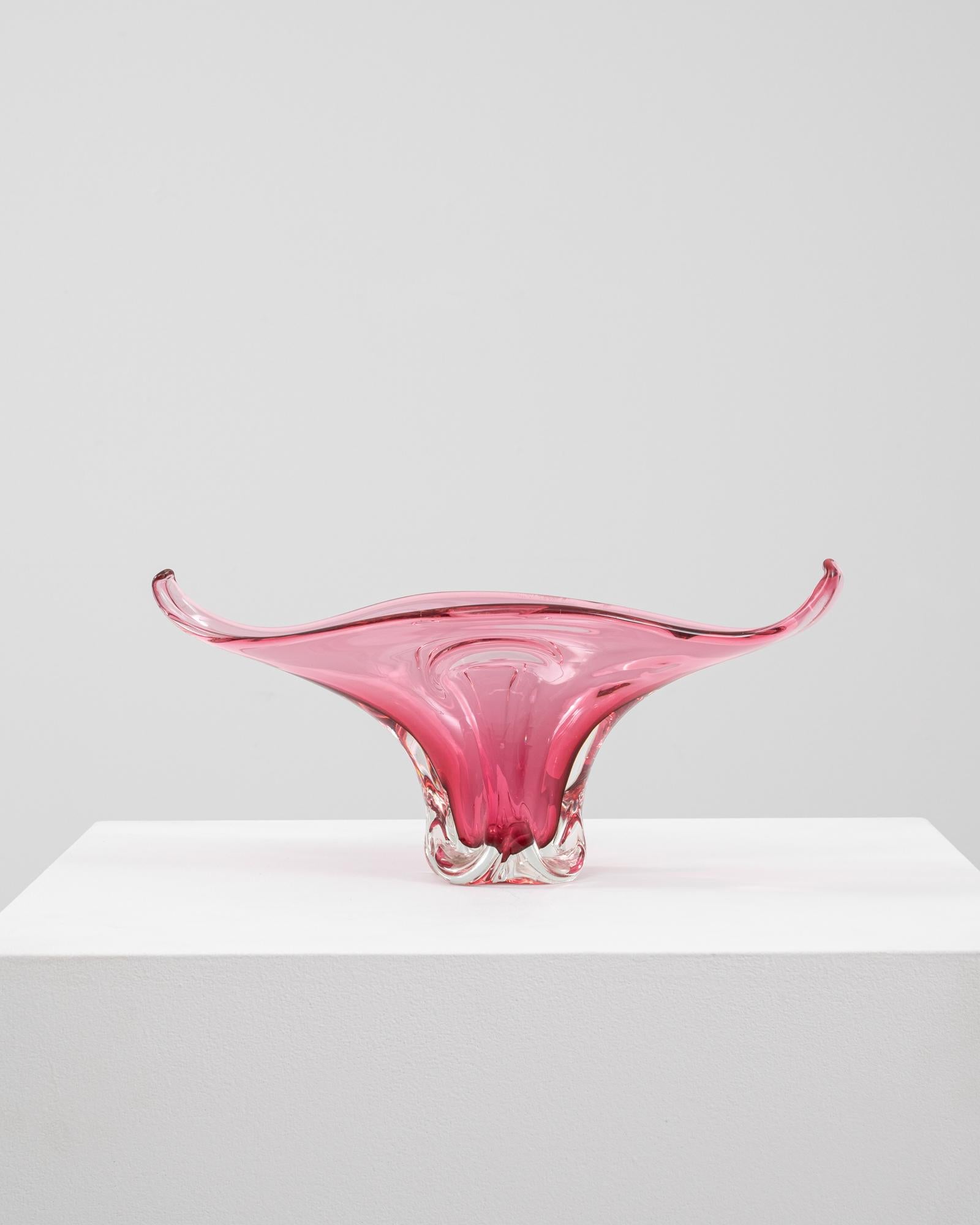 This 20th Century Italian glass vase is a stunning display of Murano-style craftsmanship, featuring a radiant pink hue with a clear base that enhances its luminous quality. The vessel’s elongated, wing-like arms sweep upward in a dramatic curve,