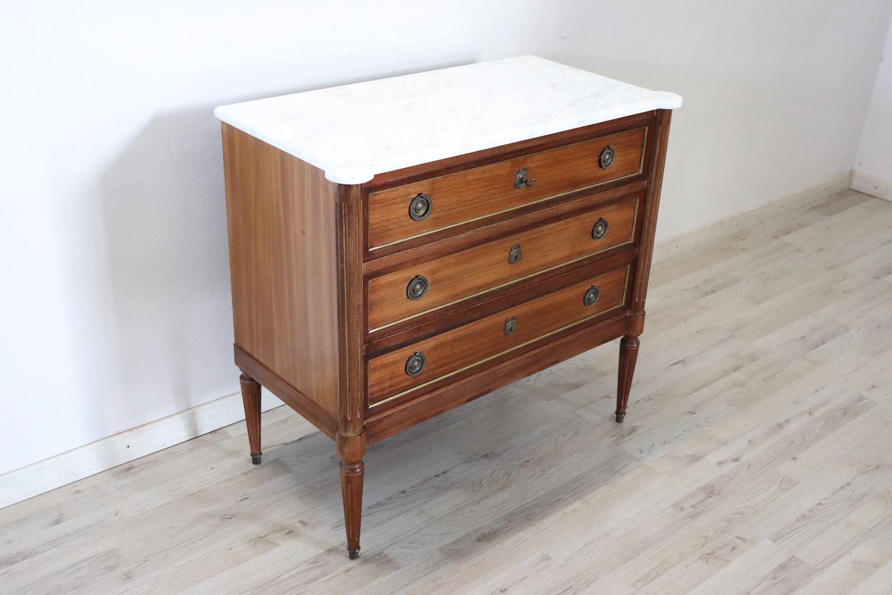 Particular small antique Louis XVI style dresser made in the early decades of the 20th century. Very elegant mahogany with characteristic profiles in fine golden brass, white marble top with shaped corners that follow the line of the dresser. On the