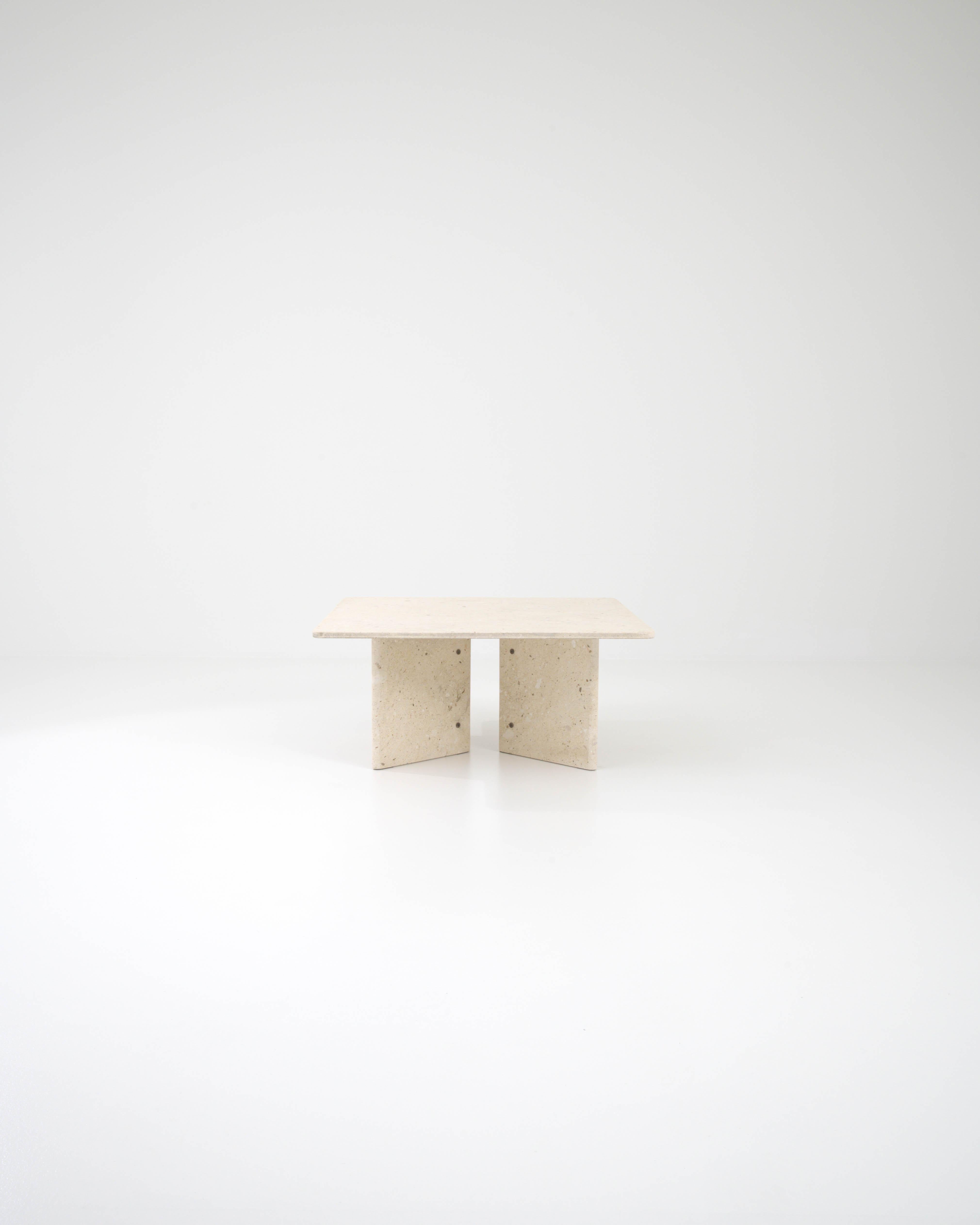 This sculptural table, crafted from cream colored marble in 20th century Italy, features a square slab as its tabletop, elegantly elevated on stone blocks. These blocks are artfully assembled like an open book and secured with metal rings, resulting