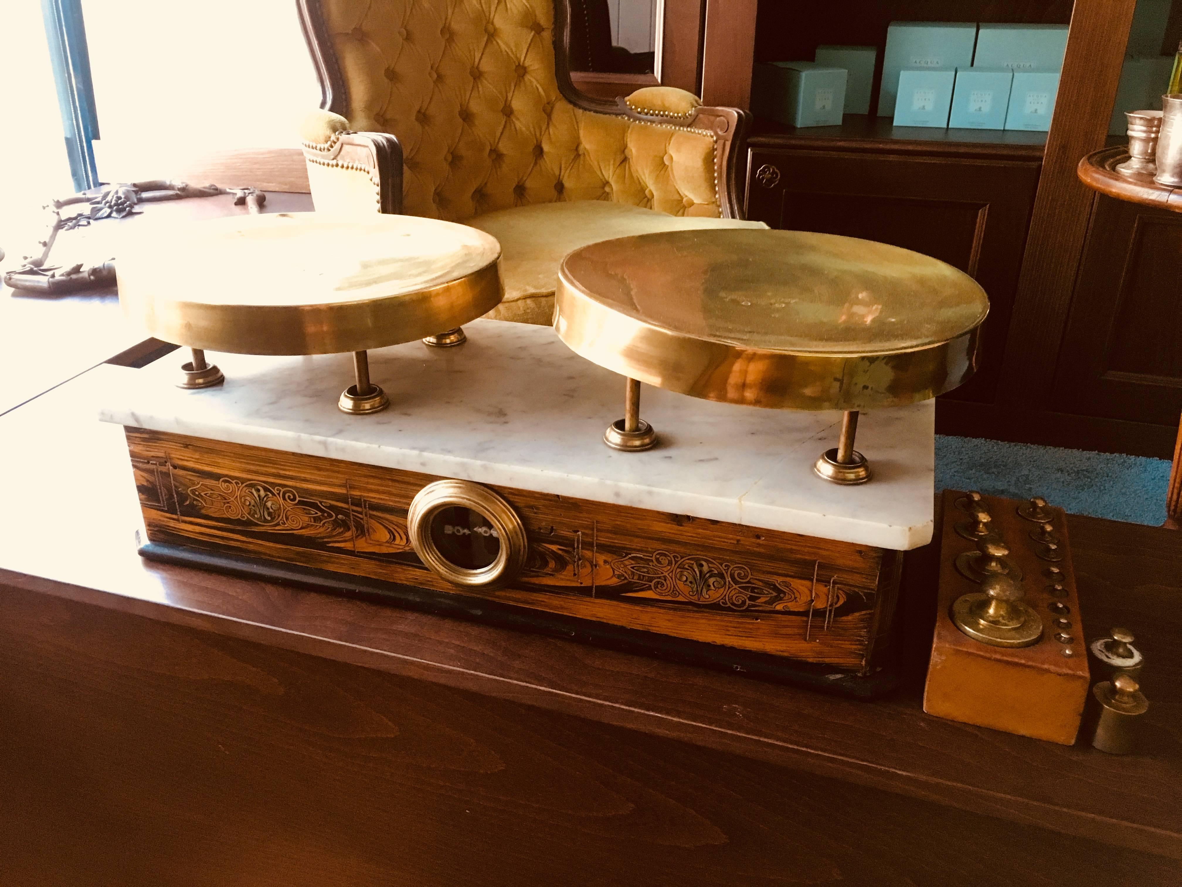 Italian marble-top balance scale. White marble-top with chamfered corners, has round nickel trays on top of the balance arms and an inlaid mahogany case on brass claw feet with glass panel on the front showing the painted and nickel plated mechanism