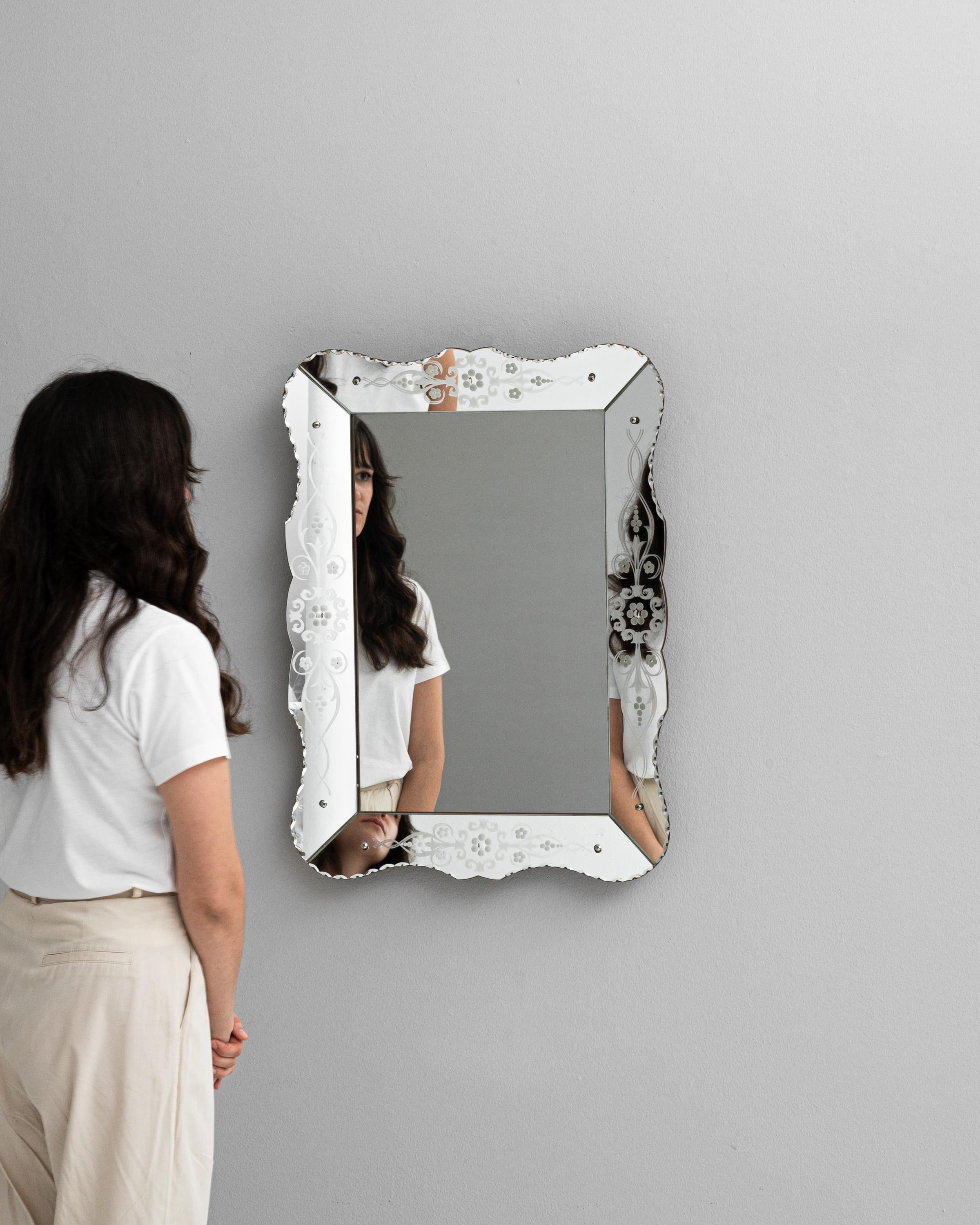 Découvrez le charme du design italien avec cet exquis miroir du XXe siècle, qui témoigne d'une élégance intemporelle. Sa surface réfléchissante, bordée d'un cadre délicatement gravé et orné de subtils motifs floraux, capture non seulement votre