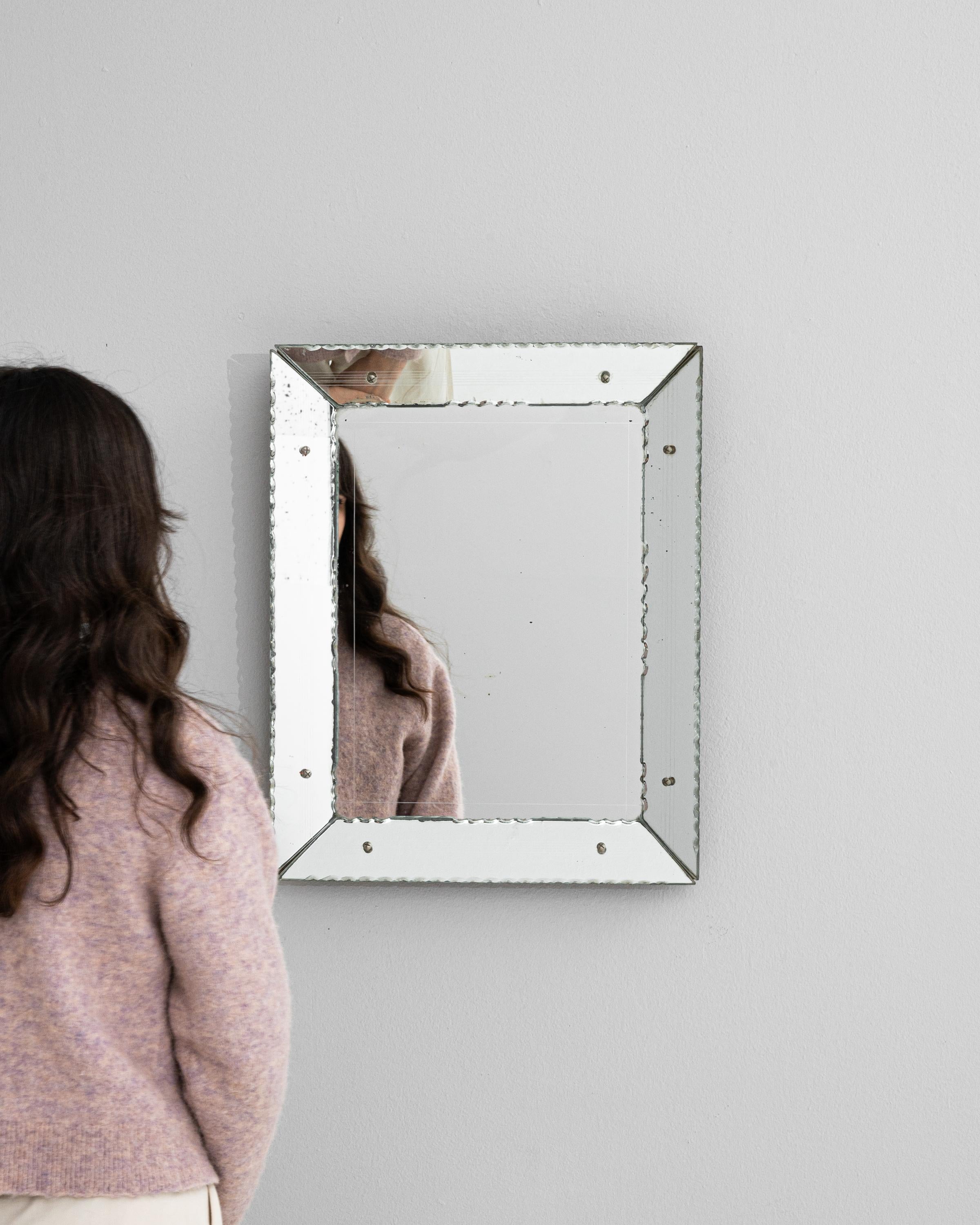 This 20th Century Italian Mirror is a quintessential example of timeless design blended with functional art. The sleek, square frame, adorned with distinctive screw caps, presents a clean, industrial aesthetic while paying homage to the mirror's