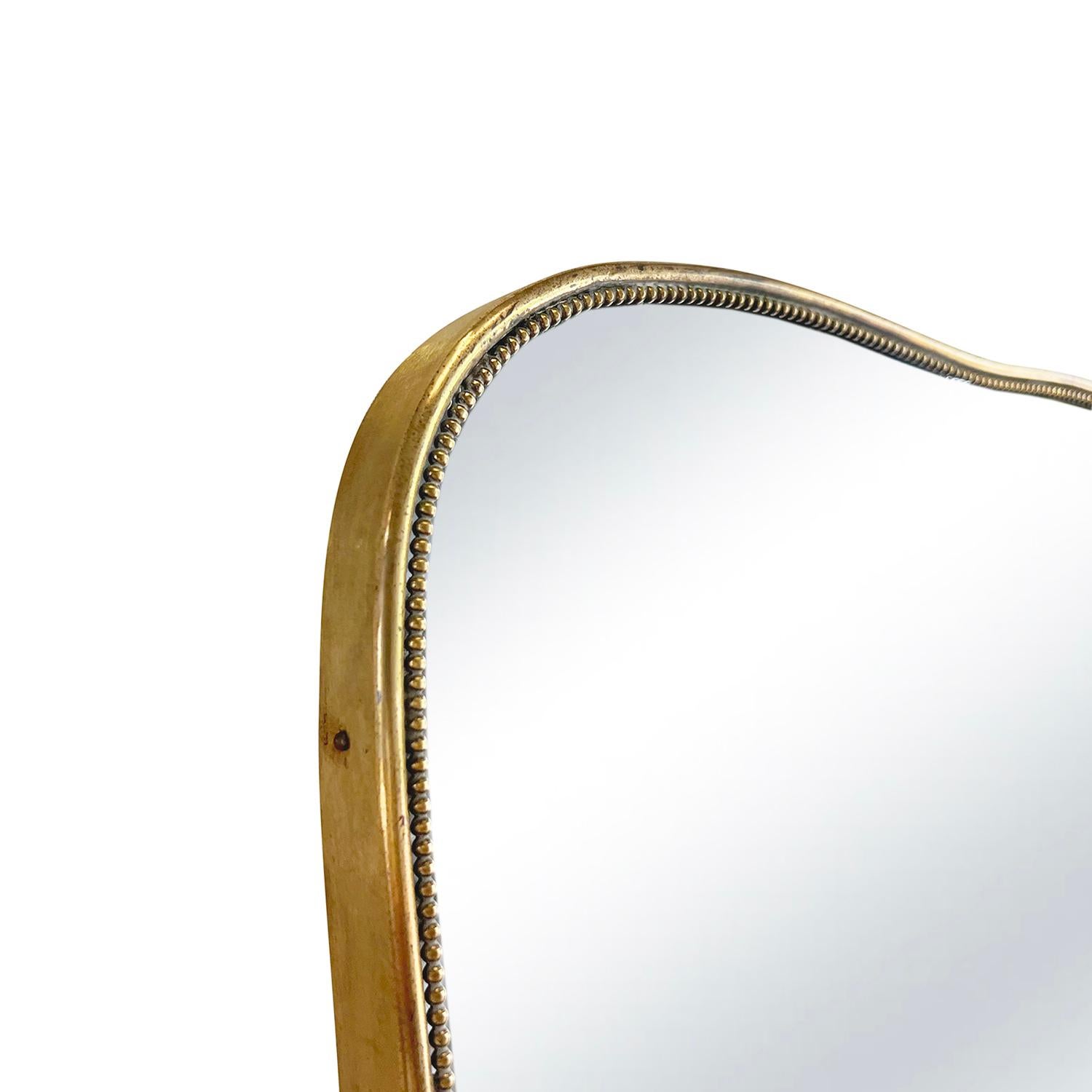A vintage Mid-Century modern Italian wall mirror with gently arched rounded tops and bottoms, made of hand crafted polished brass in good condition. The modernist mirror is particularized by many round brass heads, consisting its original mirrored