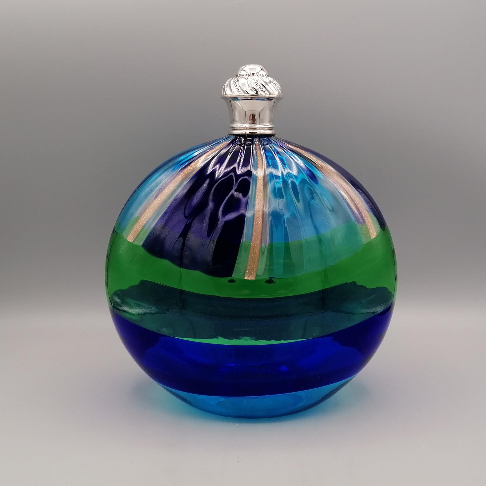Mouth-blown Murano glass bottle,
with blue, green and blue polychrome colors.
The shape is rounded oval
In the upper part there are 6 strips with inserts in pure gold dust.
The bottle cap is in silver and hand chiseled with a tochon design and the