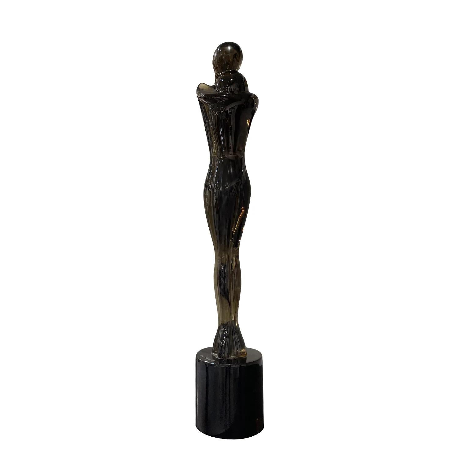 A vintage Mid-Century Modern Italian large sculpture of a hugging, loving couple made of hand blown smoked Murano glass, designed by Pino Signoretto in good condition. The detailed décor piece is resting on a round black base, representing a woman